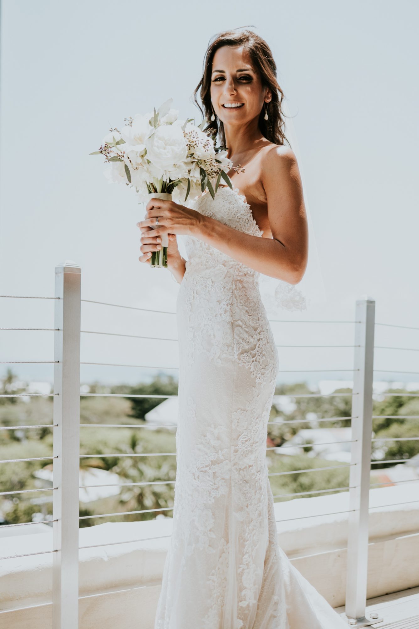 A bride in a white wedding dress standing on a rooftop balcony overlooking the ocean, captured by Key West Wedding Photographer.