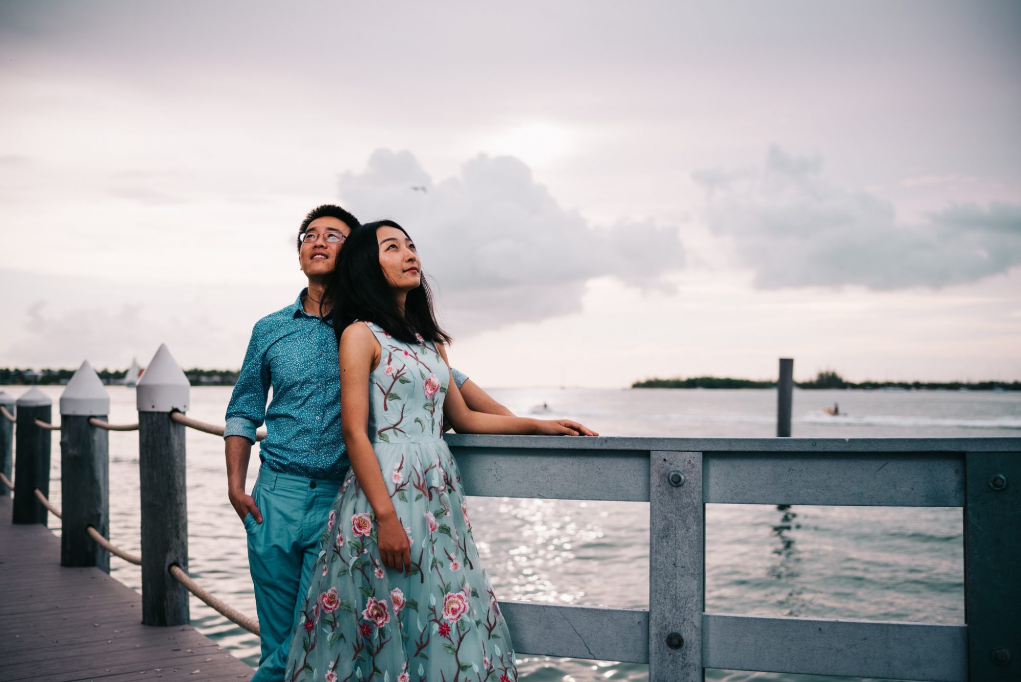 A couple standing on a pier near the ocean during a sunset engagement session in Key West, FL.