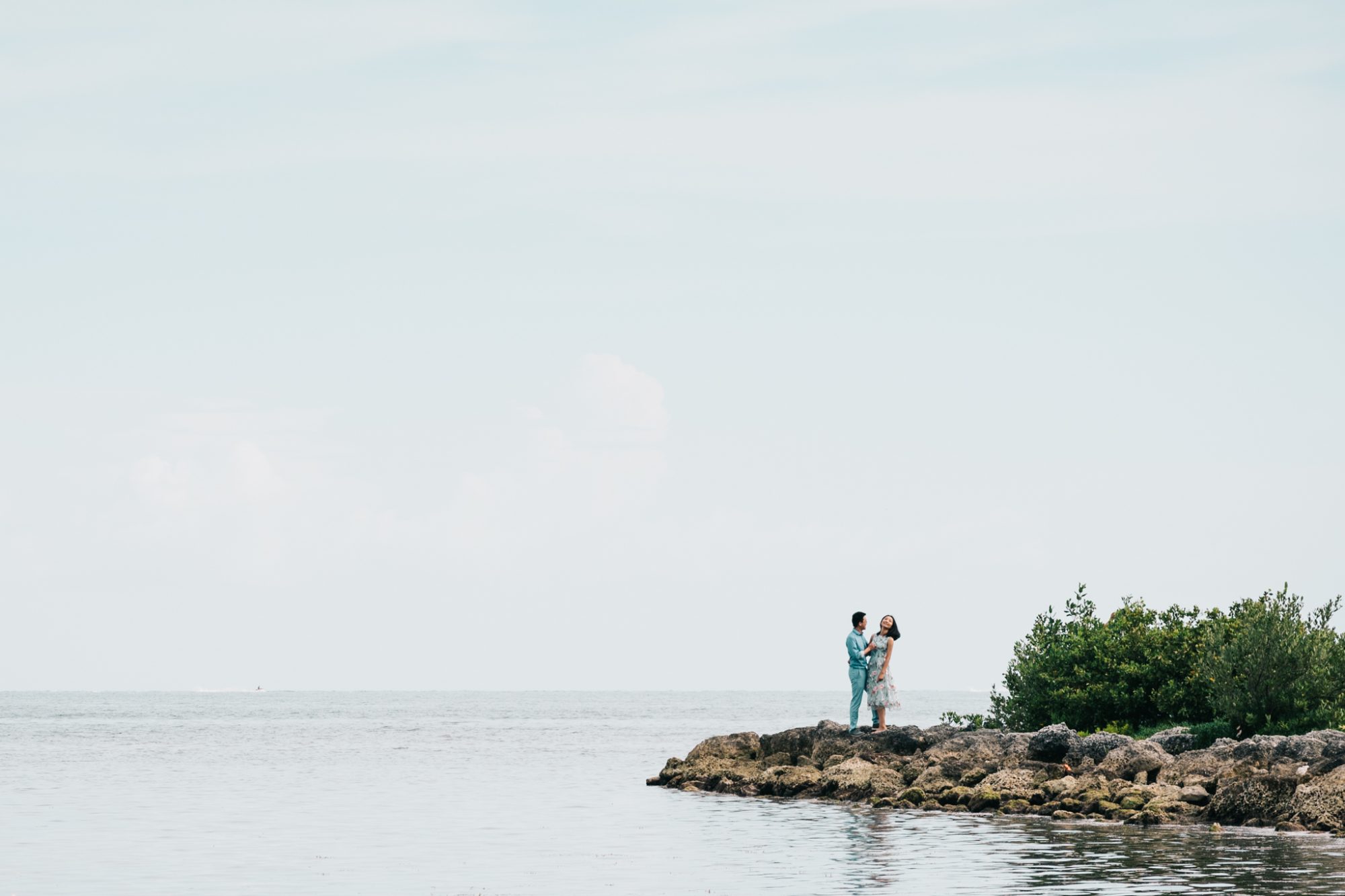 A couple's sunset engagement session in Key West, FL, featuring Xiao and Ying standing on a rock in the water.