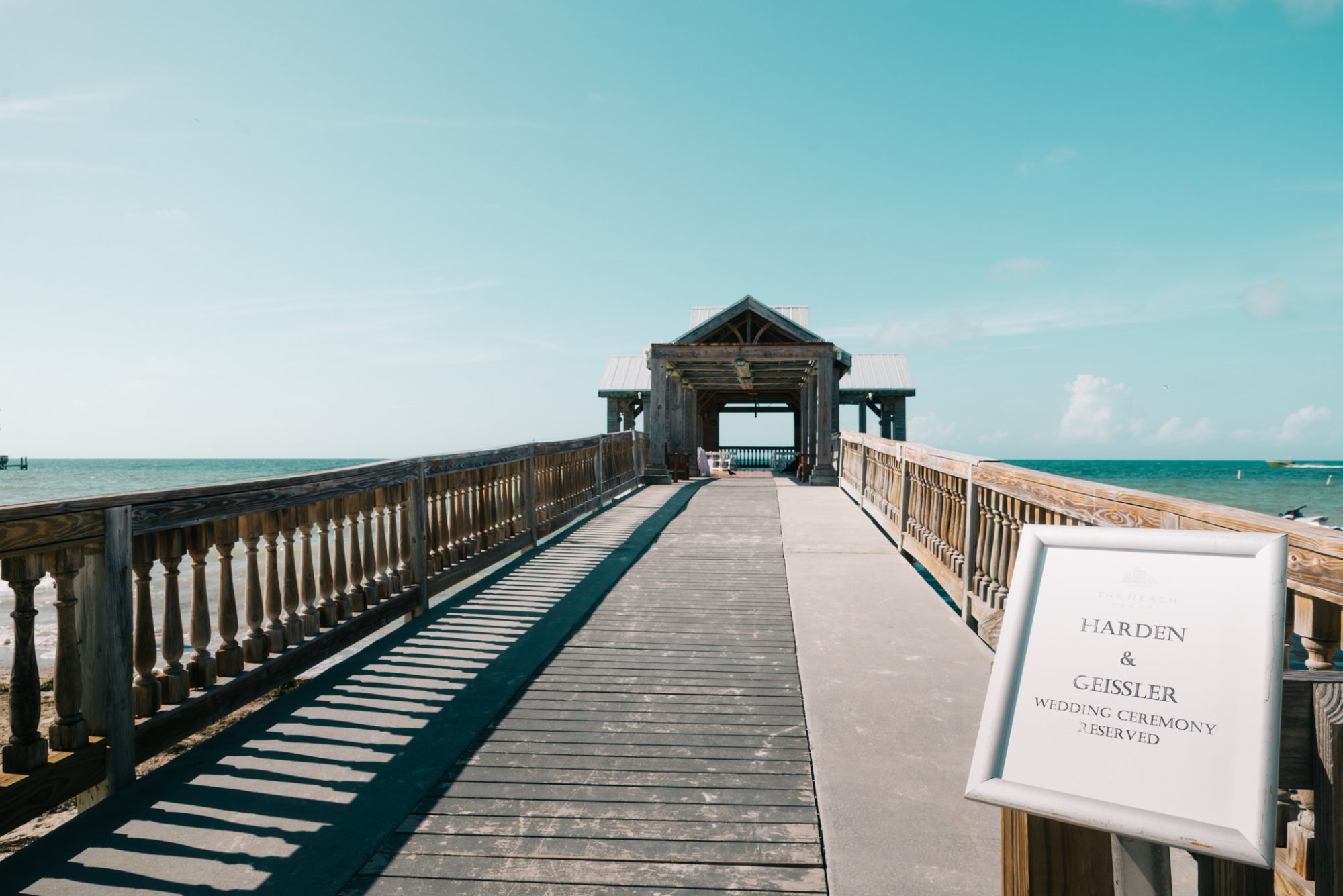 A wooden pier with a sign on it next to the ocean at Reach Resort capturing Stacy and Jason's Key West wedding.
