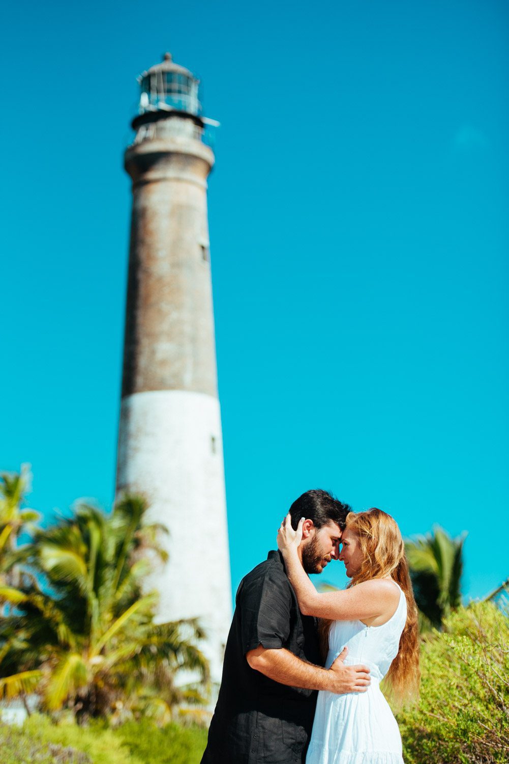 An engaged couple embracing in front of a picturesque lighthouse during their destination engagement session at Dry Tortugas.