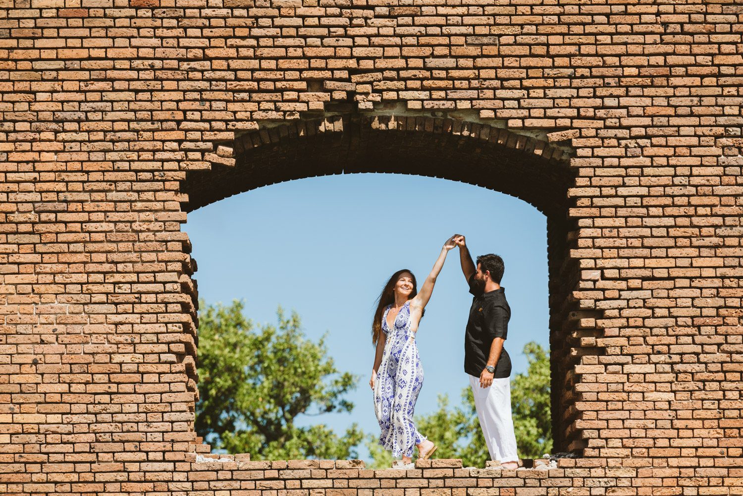 A man and woman standing in a brick archway during their destination engagement session.