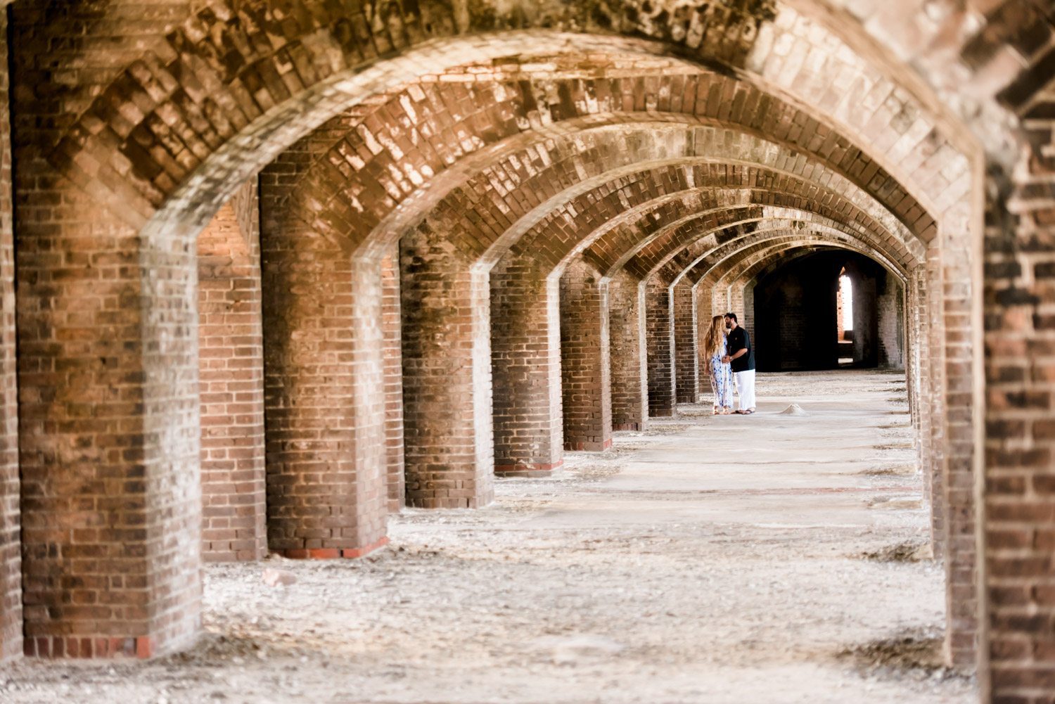 A couple in a destination engagement session, walking down an archway in the old fort of Dry Tortugas.