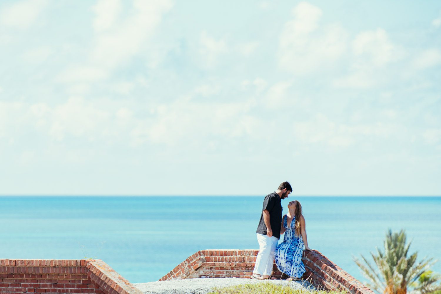 A couple having a destination engagement session, standing on a wall overlooking the ocean at Dry Tortugas.