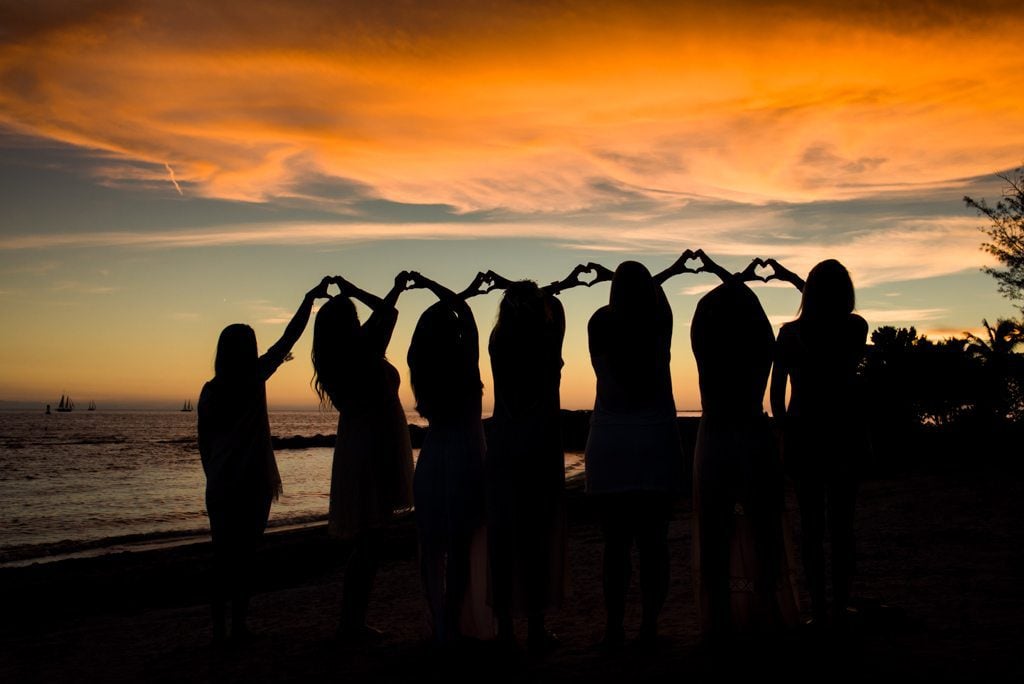 A group of girls holding hands in front of a sunset during a Bachelorette Party Weekend in Key West.