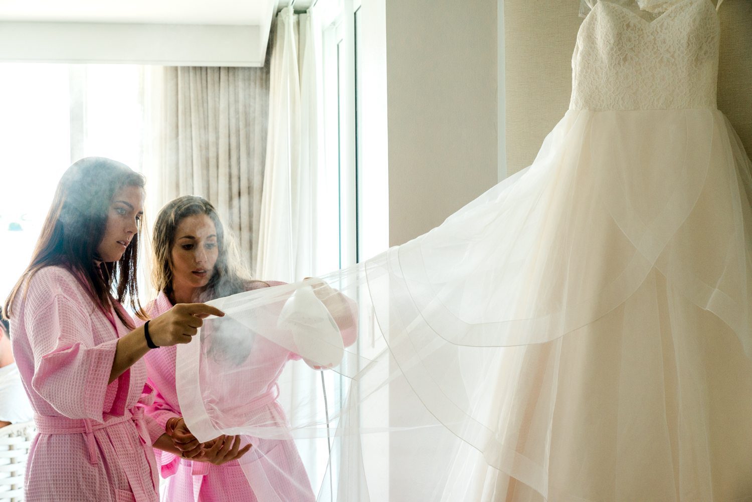 Two key west bridesmaids in pink robes looking at a wedding dress.