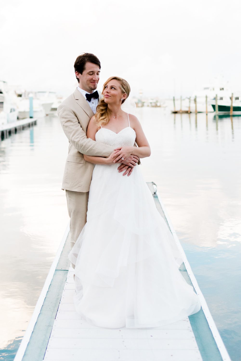 A key west wedding with the bride and groom standing on a dock in front of a boat.