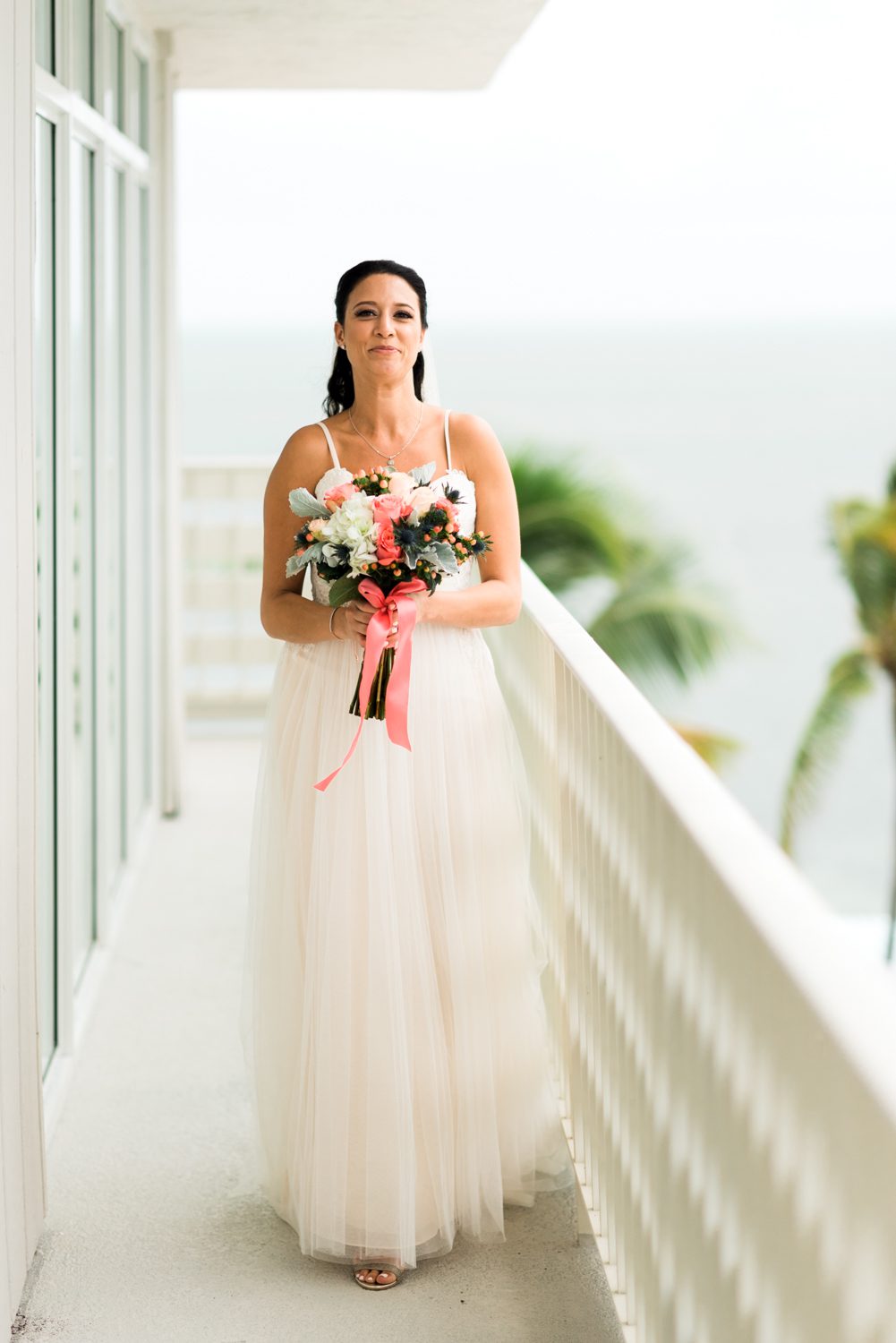 A bride holding a bouquet on a balcony overlooking the Florida Keys.