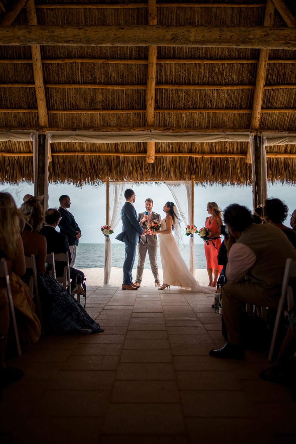A bride and groom standing under a thatched gazebo at a Florida Keys wedding beach venue.