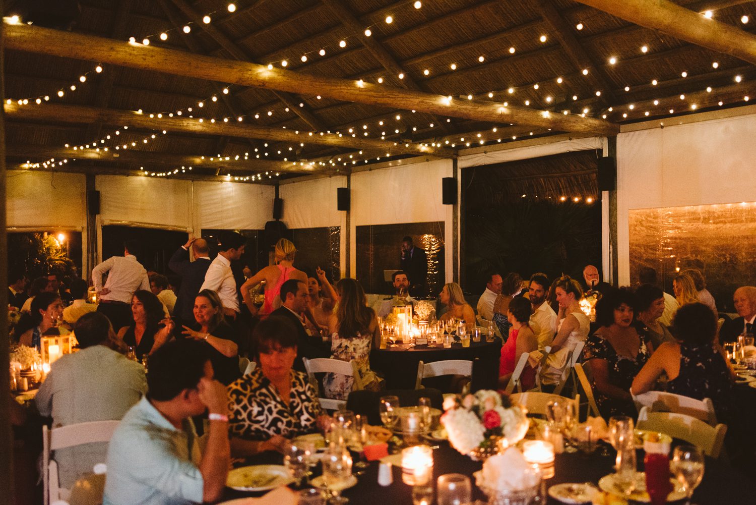 A Florida Keys wedding reception with people sitting at tables under string lights at the Postcard Inn.