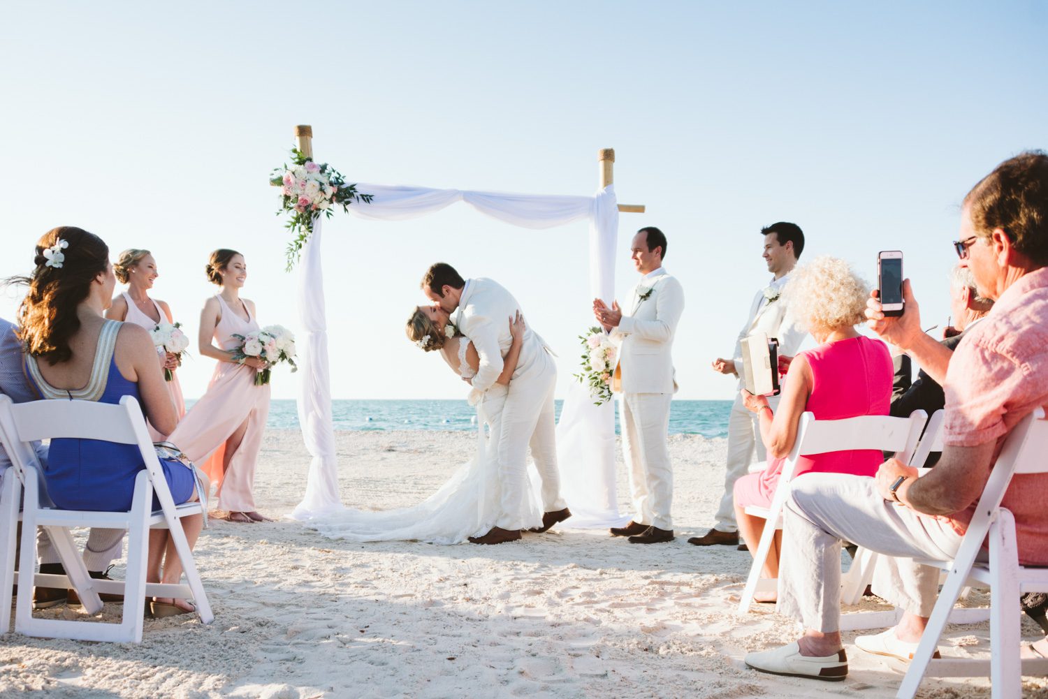 A sunset wedding ceremony on the beach in Key West with a bride and groom kissing.