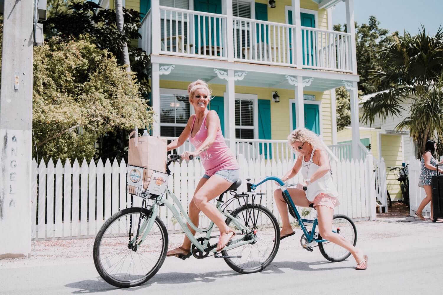 Two women riding bikes in front of a house in Key West, captured by Kristina & Forrest, the Fort Zachary Taylor wedding photographers.