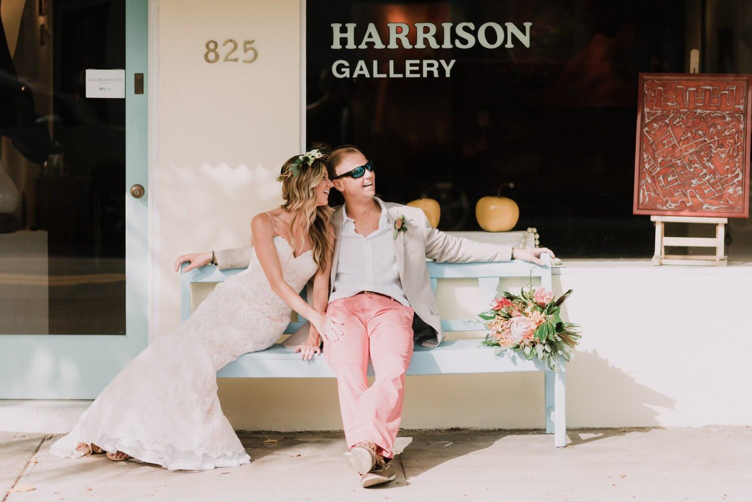 A bride and groom sitting on a bench in front of the Harrison Gallery at Fort Zachary Taylor, captured by Key West Wedding Photographer.