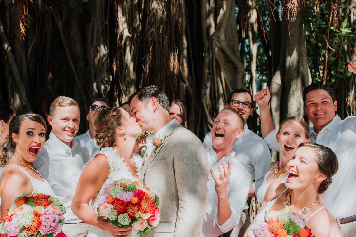 A group of bridesmaids and groomsmen kissing in front of a tree at an Ocean Key Resort Spa Wedding in Key West.