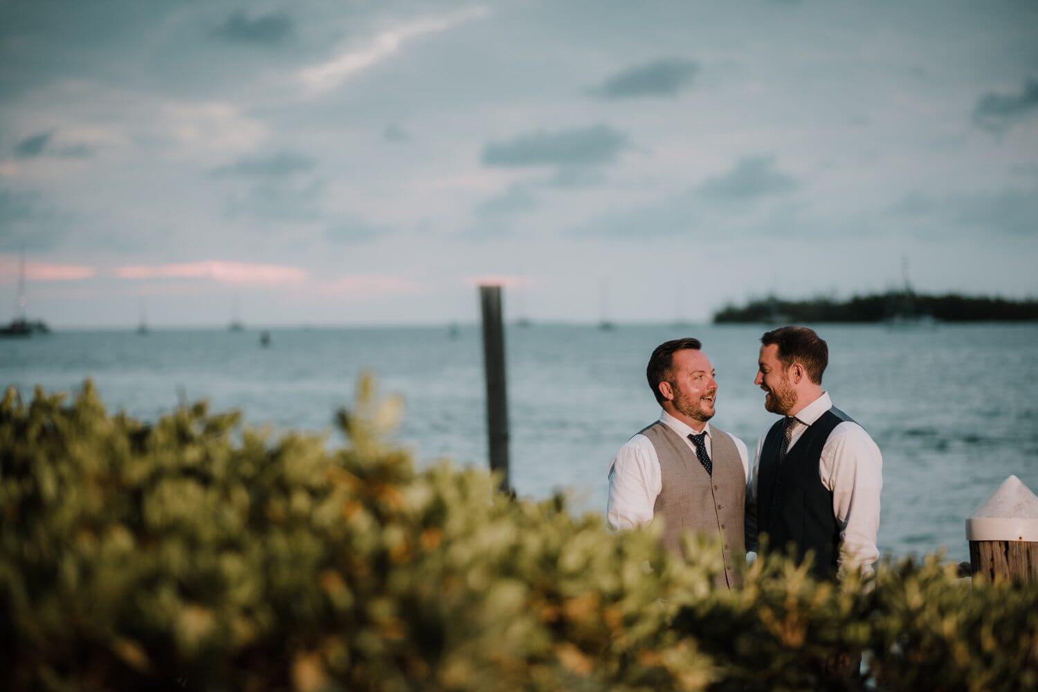Two grooms standing next to each other in front of the water at a Key West wedding.