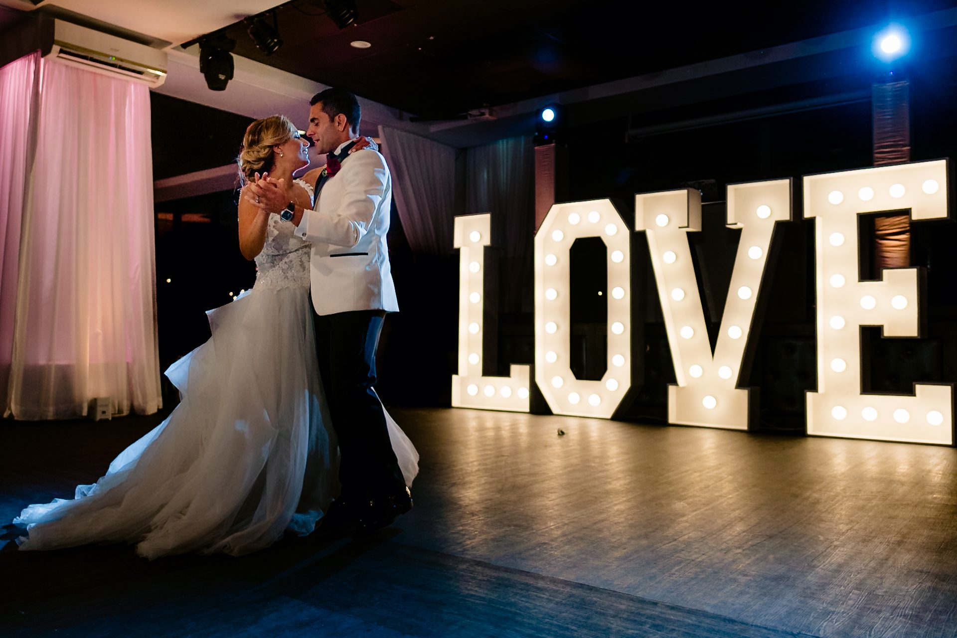 A Miami wedding with a bride and groom standing in front of a lit up love sign.