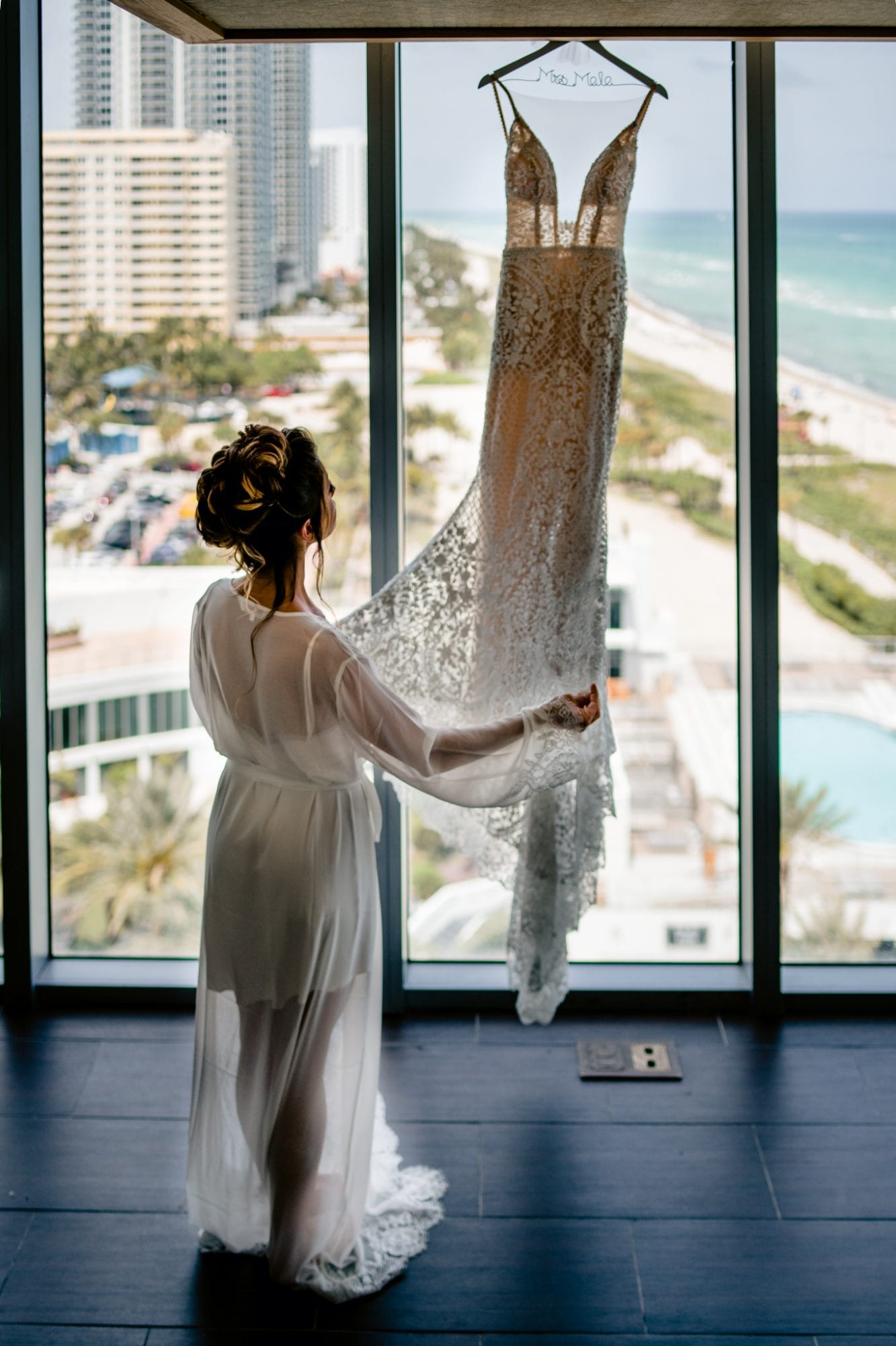 A bride hangs her wedding dress in front of a window overlooking the ocean at Eden Roc Resort in Miami.