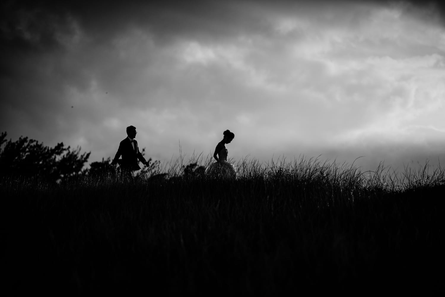 Two people walking on a hill under a cloudy sky.