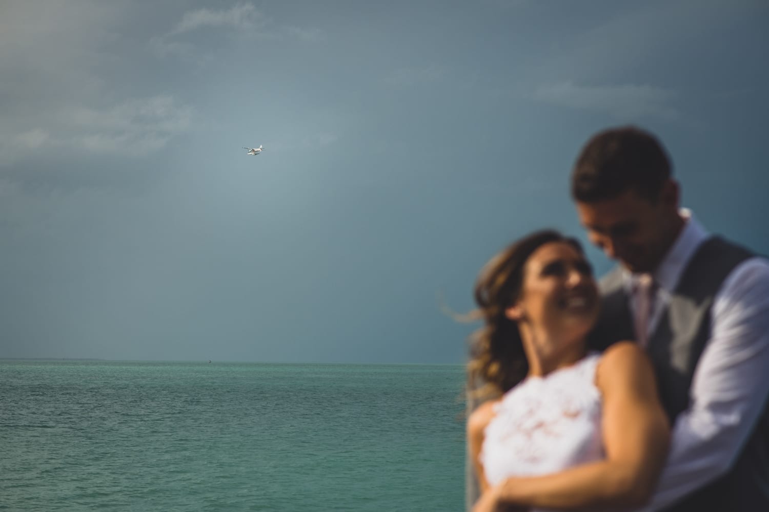 A bride and groom embracing in front of the ocean.