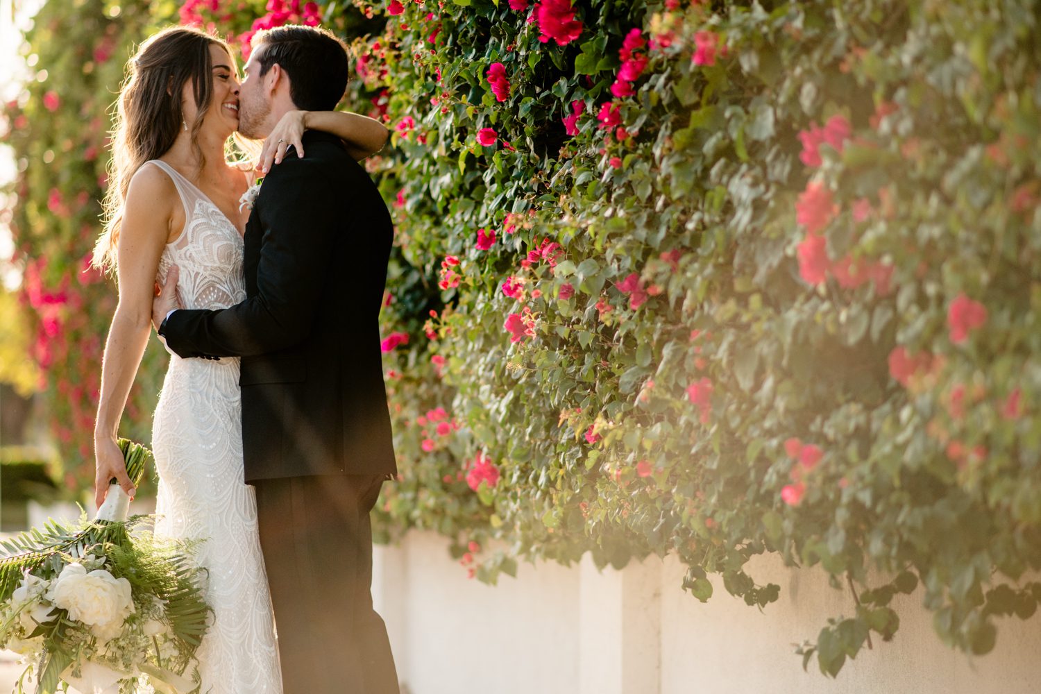 A Shana and Patrick's wedding at Hemingway House features a kiss in front of a flower wall.