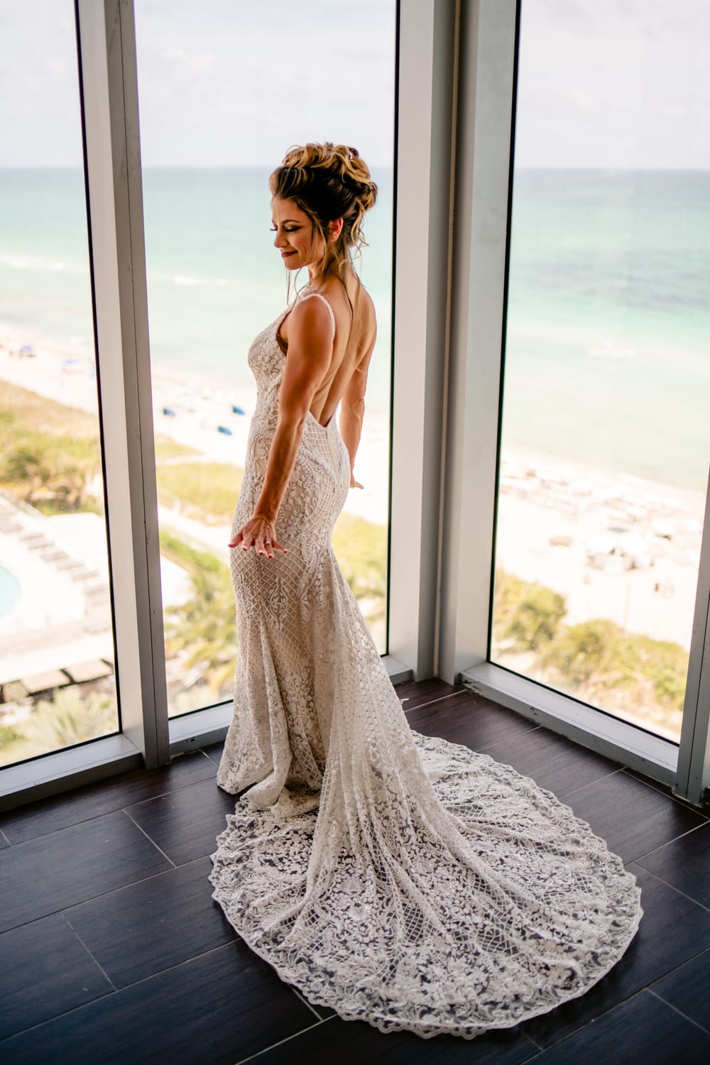 A bride in a wedding dress standing in front of a window overlooking the ocean at Eden Roc Resort in Miami.
