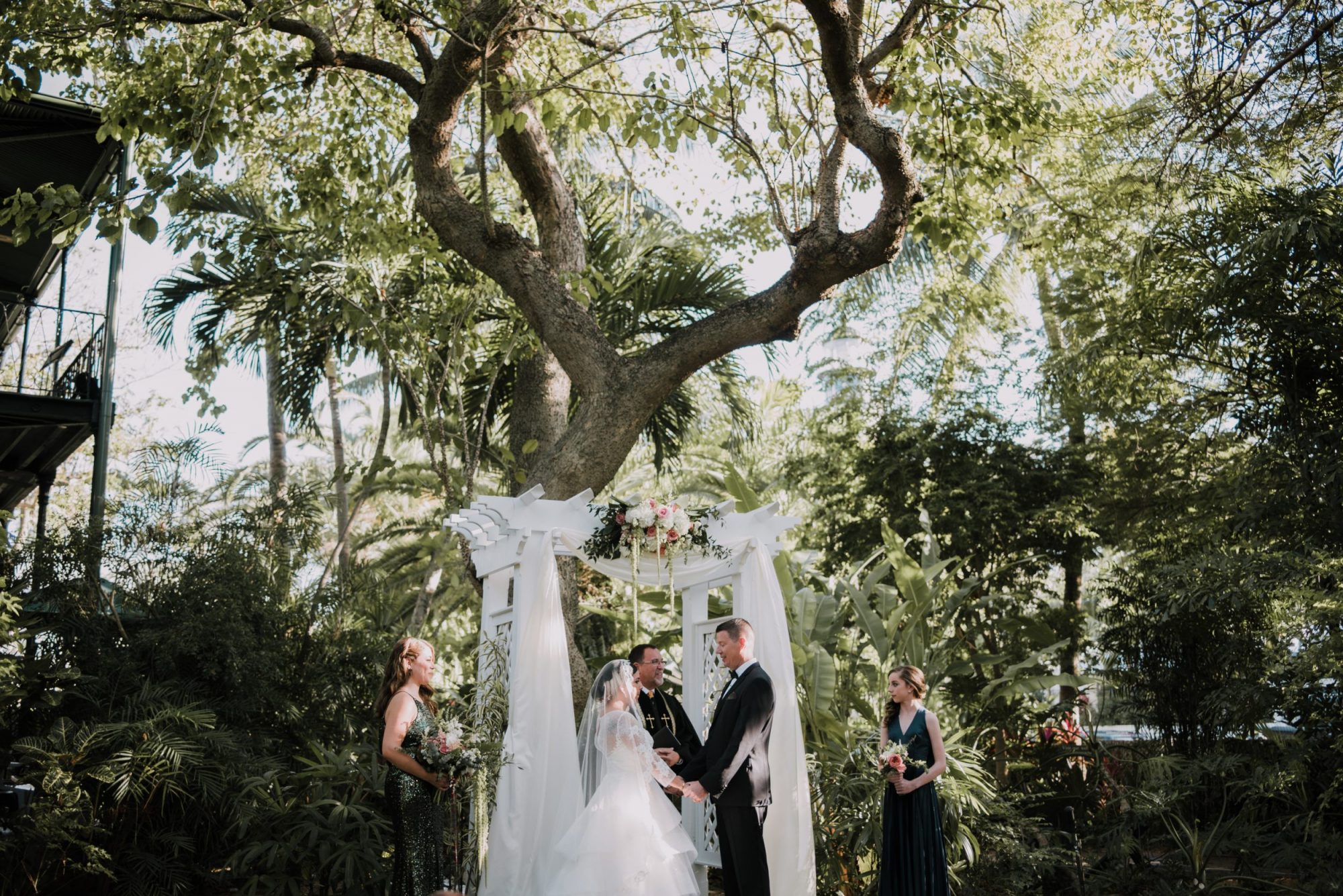 A vintage Hollywood couple standing under a tree at their Key West wedding ceremony.
