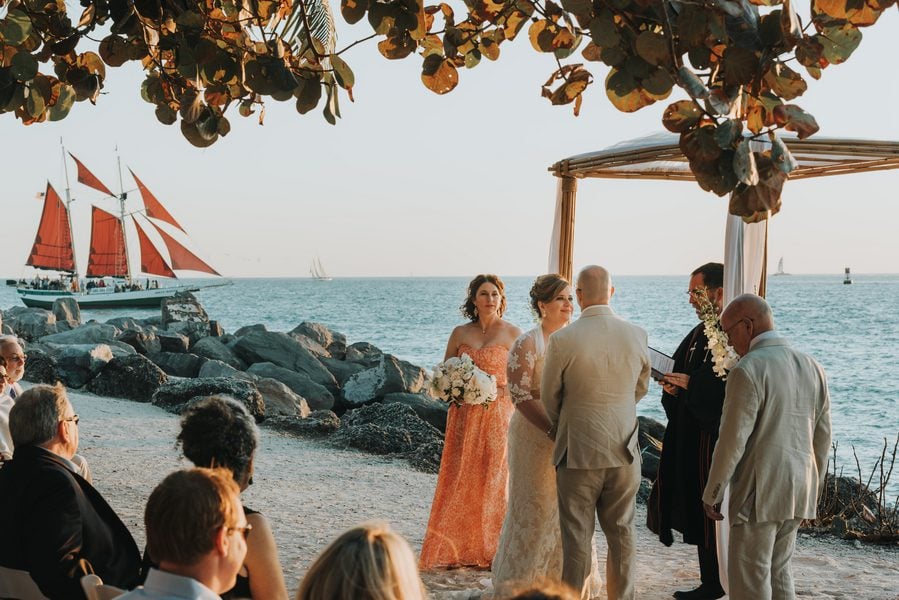 A Key West wedding ceremony on the beach with a sailboat in the background, captured by a talented Fort Zachary Taylor wedding photographer.
