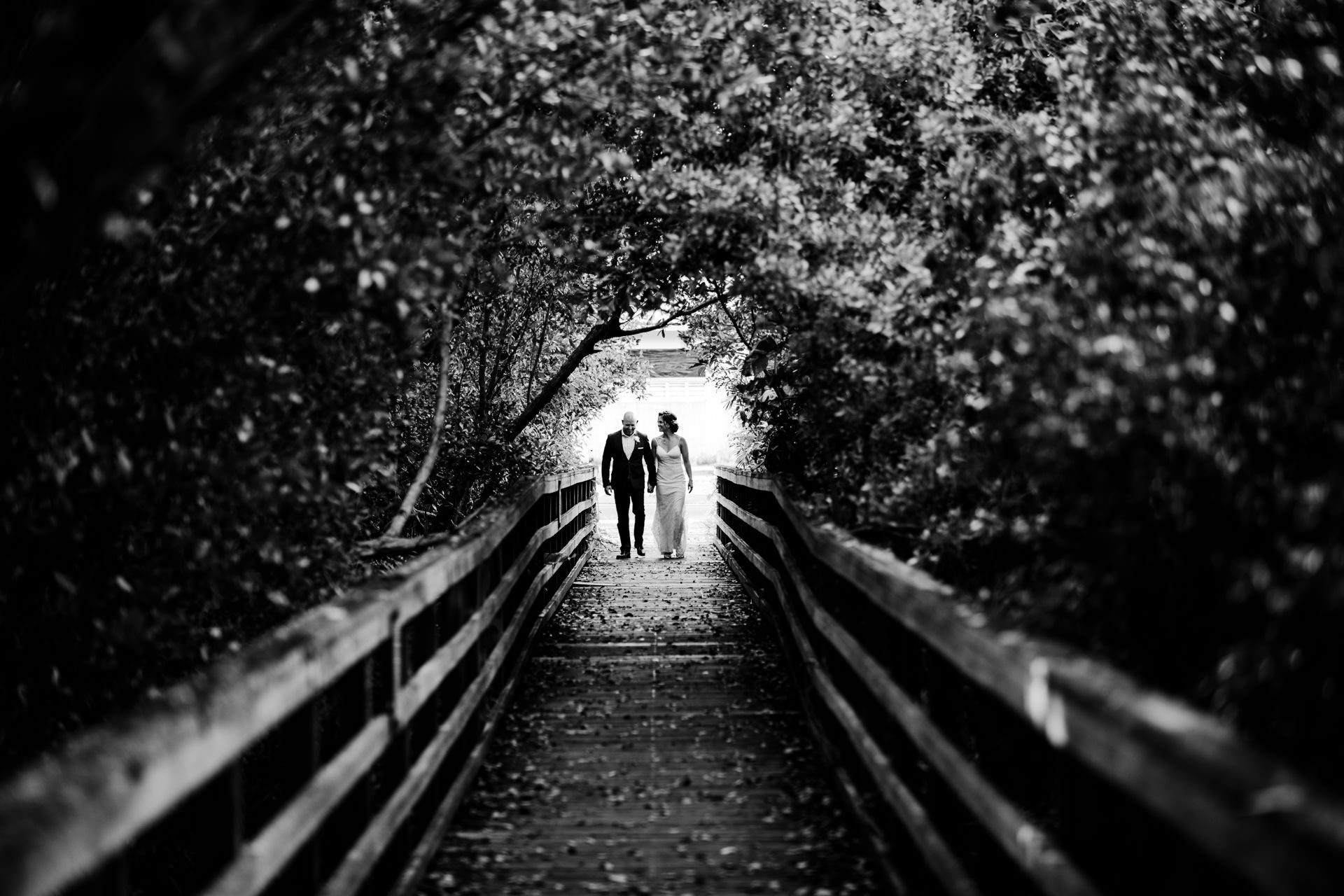 Far away shot of bride and groom walking across a wooden bridge after eloping.