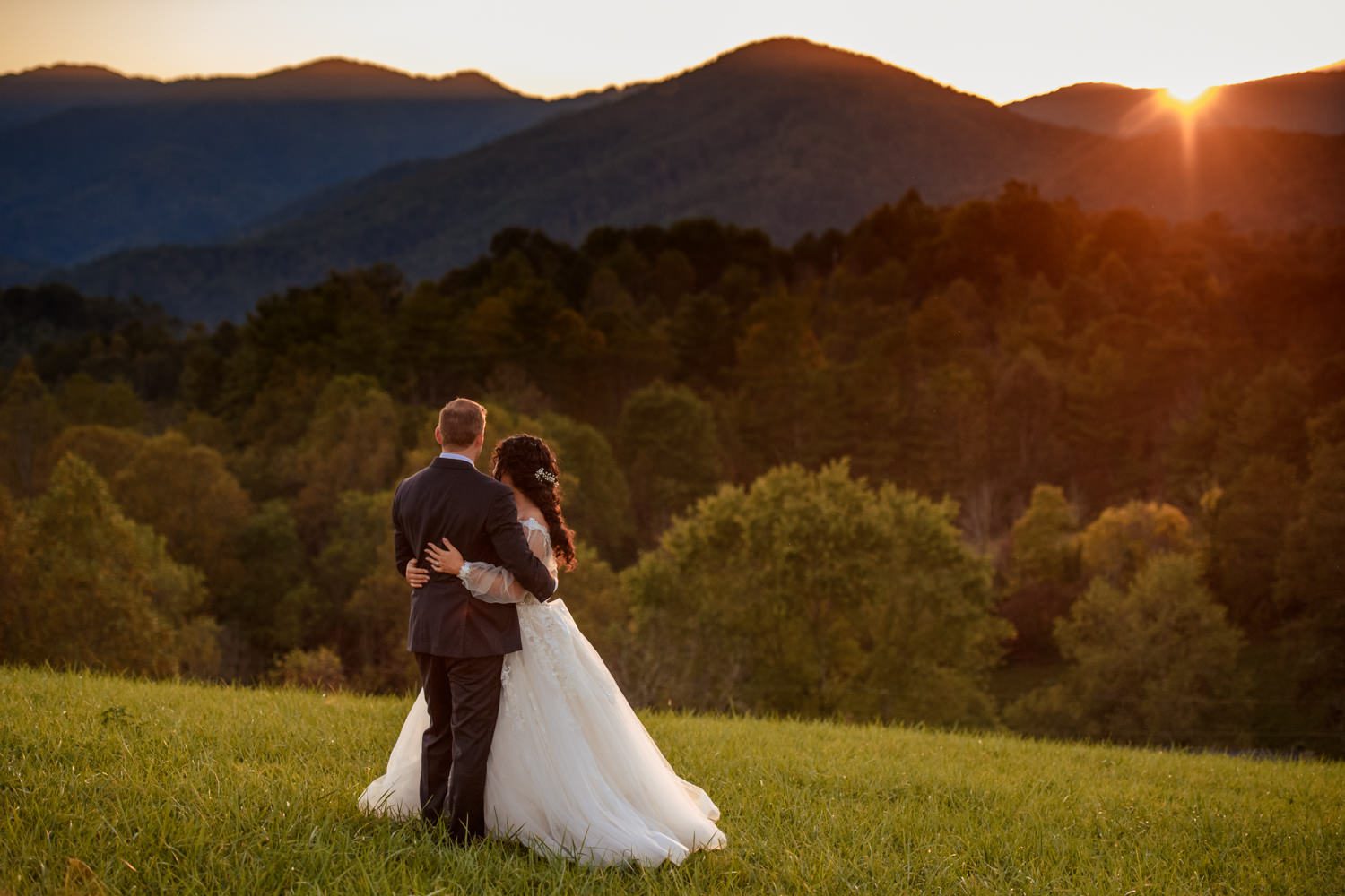 bride and groom embrace while watching the sunset from a mountain summit