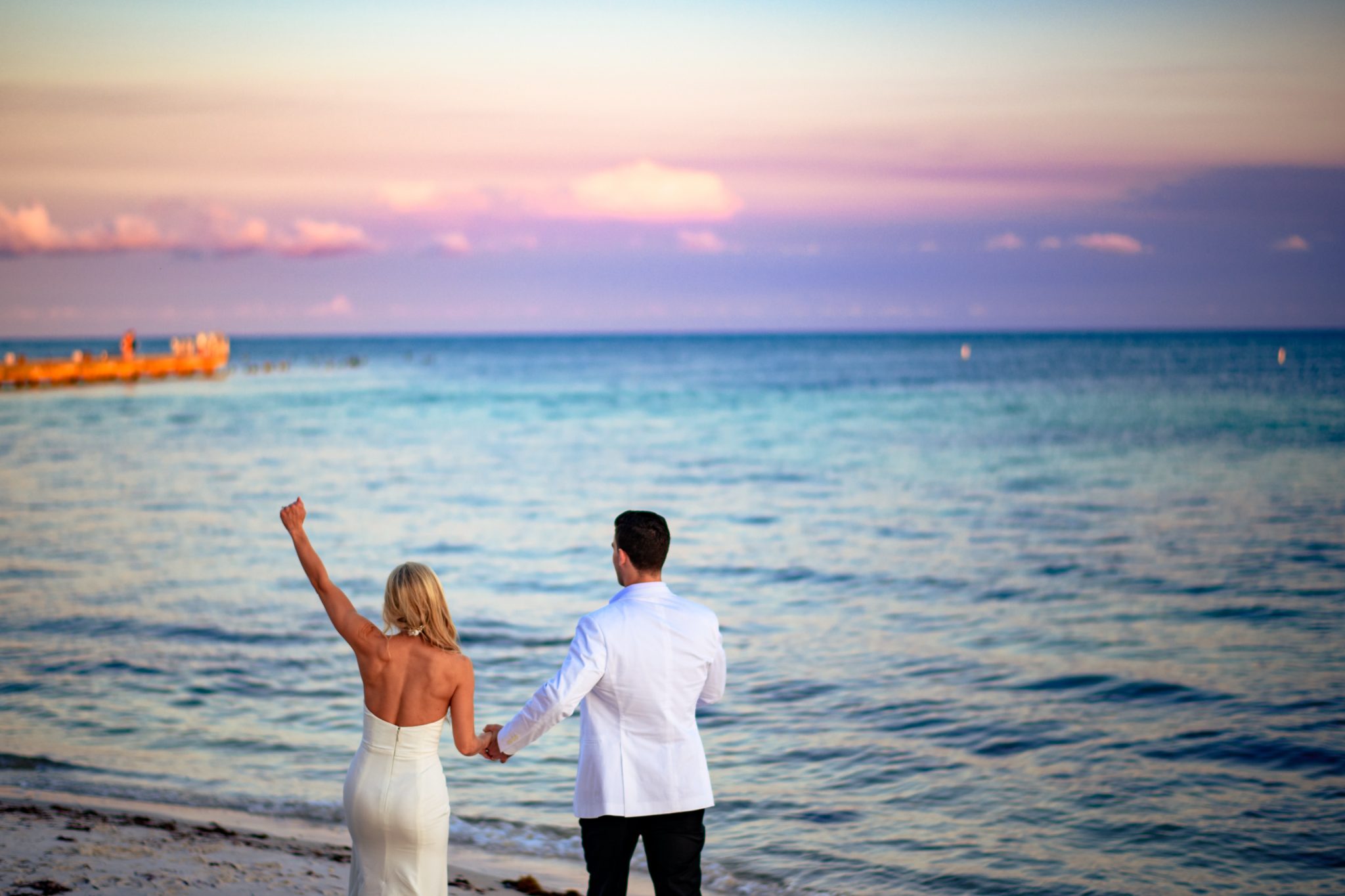 Bride holding her arm up in celebration after just being married on a beach in Key West Florida with a purple sunset