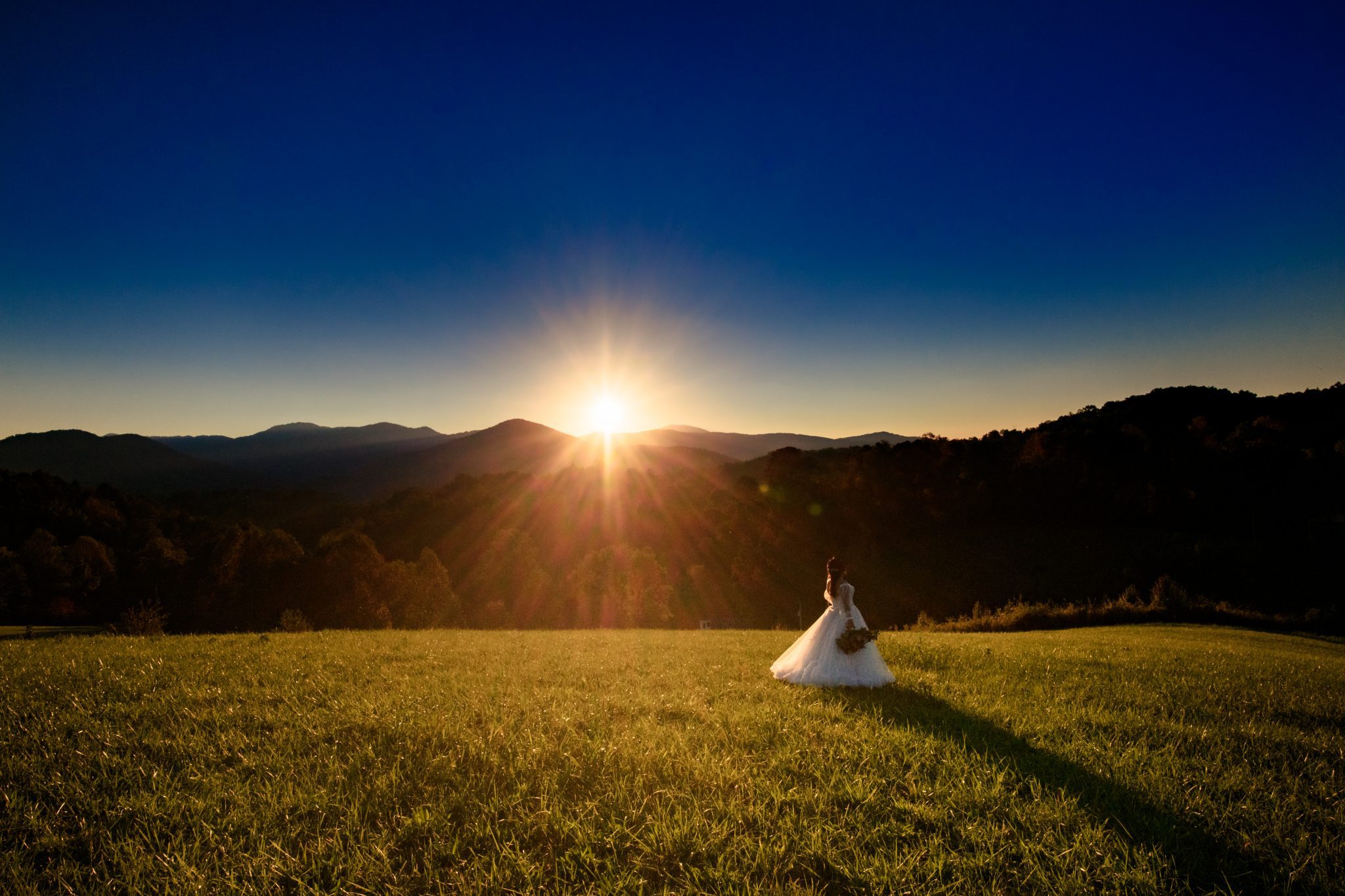 Sunset photo of bride with Ridge line behind the sun goes over the ridge line during sunset at the ridge Asheville shot while being a second photographer