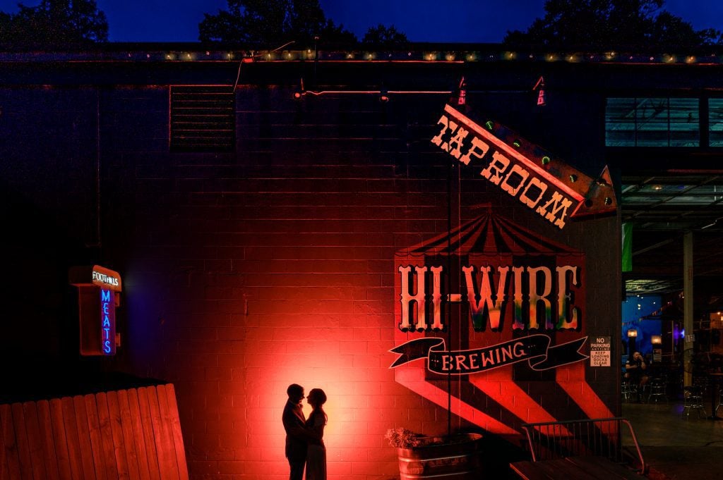 Silhouette of bride and groom standing in front of sign at hi-wire brewing tap room
