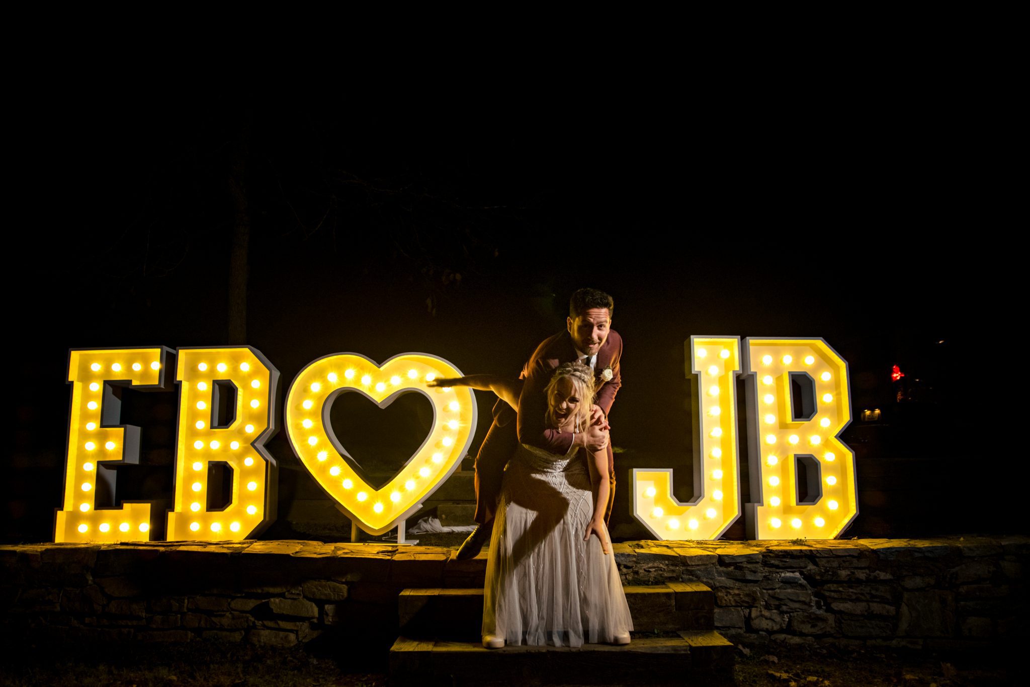 Bride and groom standing in front of light up initials at wedding