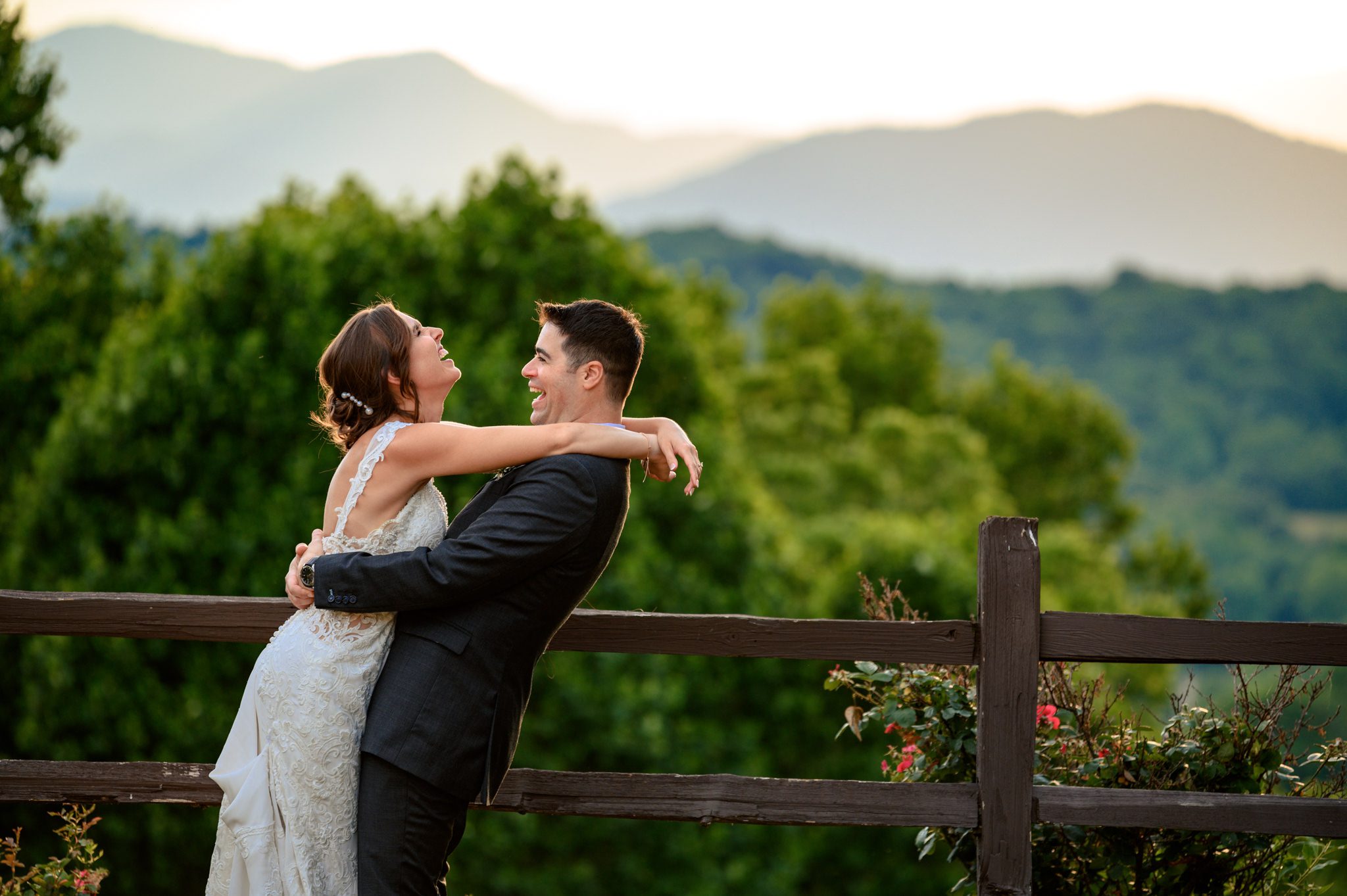 A bride and groom hugging on a fence with mountains in the background captured by a documentary wedding photographer at Crest Pavilion.
