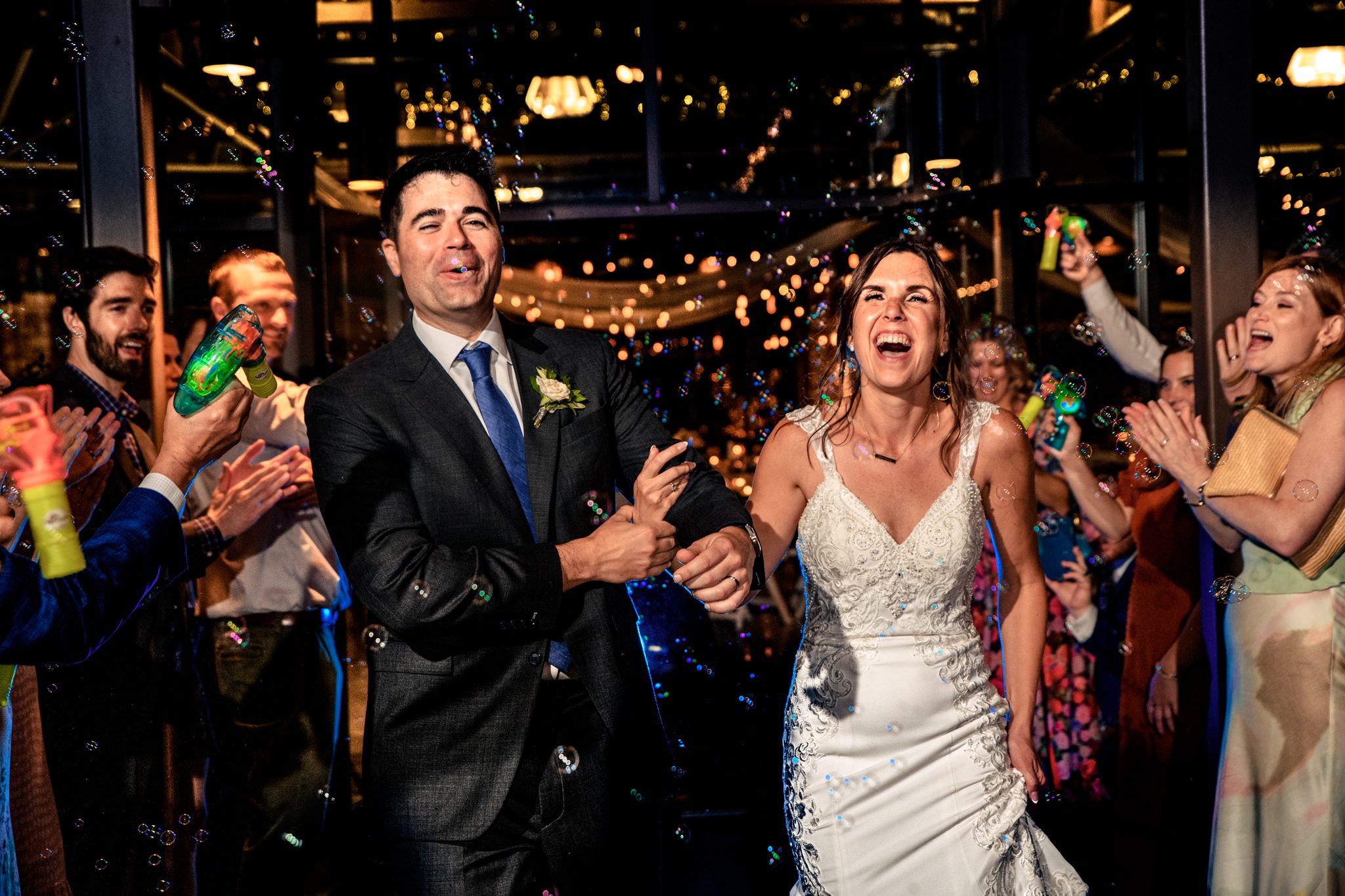 bride and groom exiting wedding reception while guests blow bubbles towards them