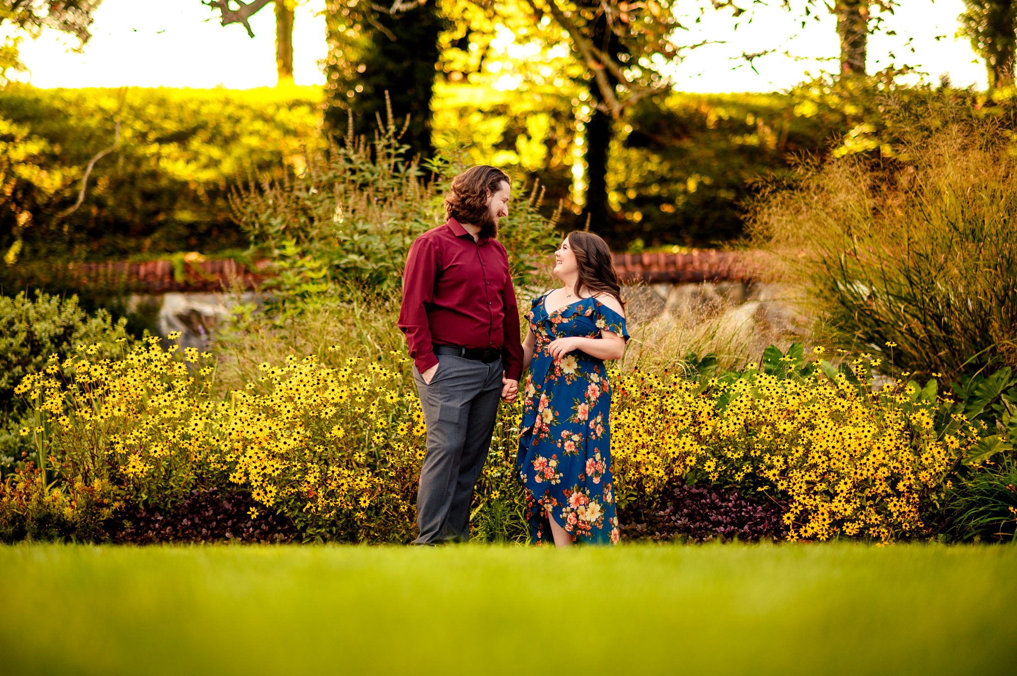 engaged couple smiling and holding hands in front of fall blooms at biltmore gardens