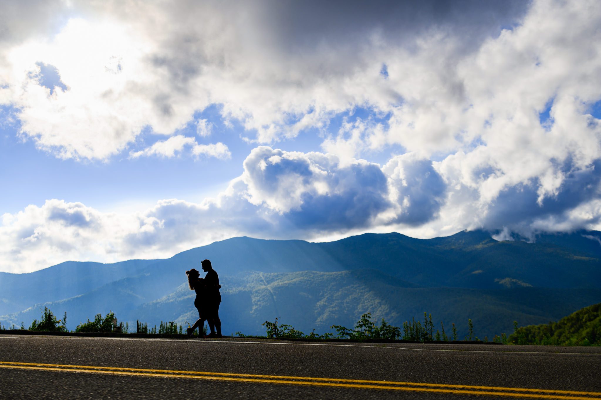 silhouette of a man and woman with rays of light over mount mitchell in the background