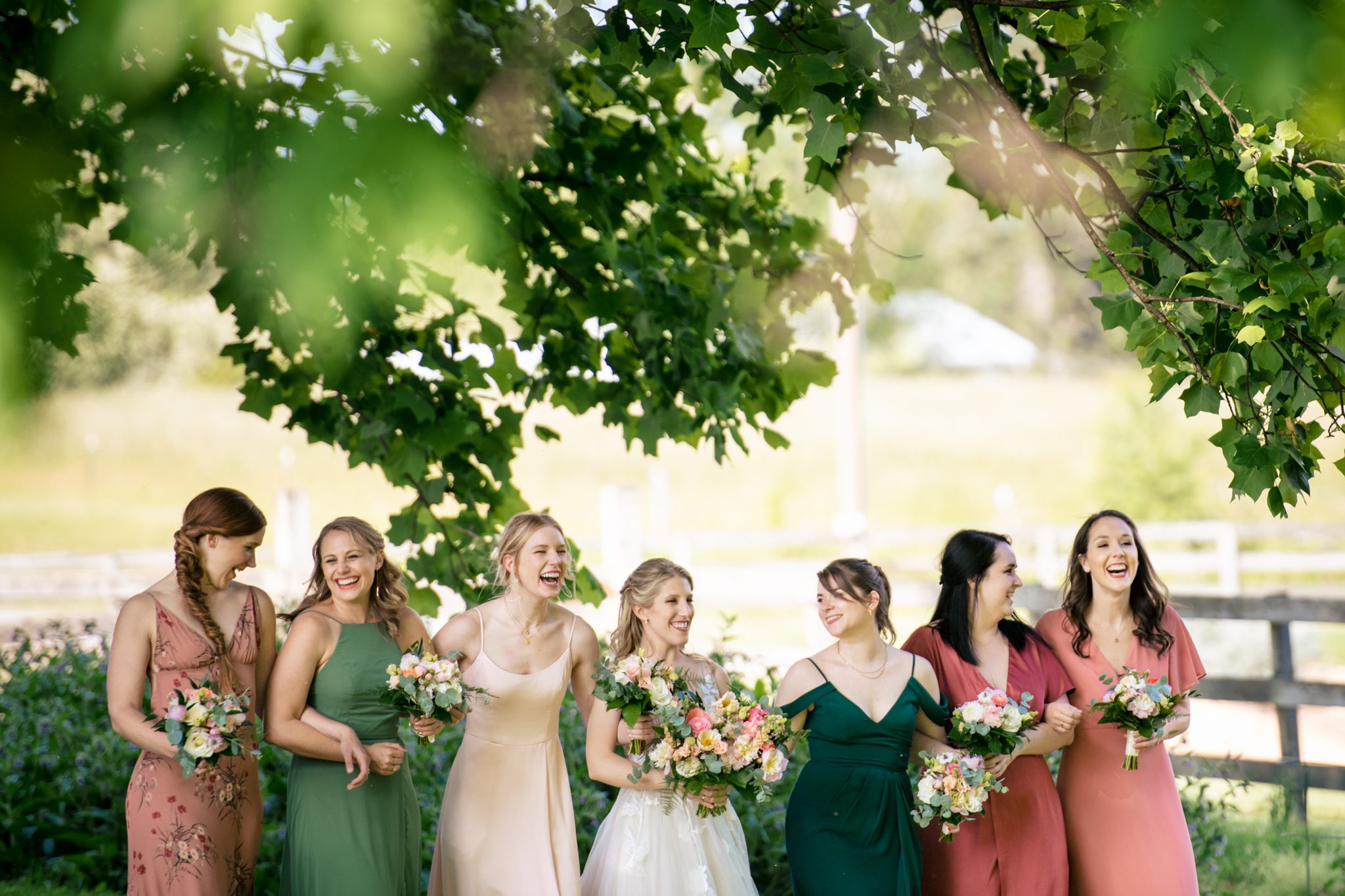 Bridesmaids strolling under a majestic oak tree at The Farm, a charming farm wedding venue nestled in Candler, NC