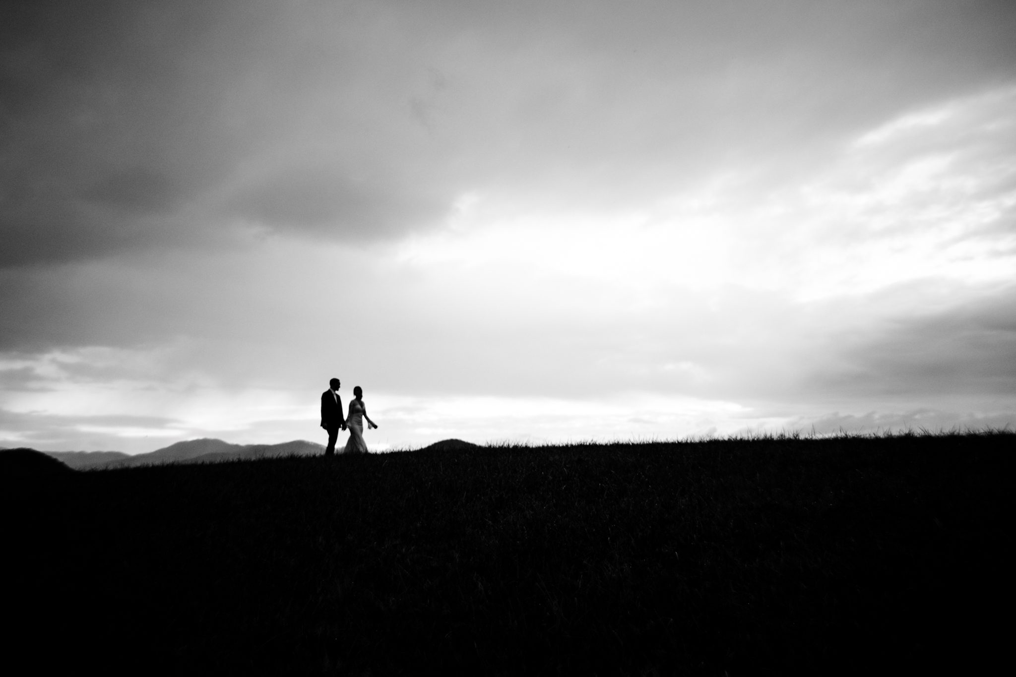 Silhouette of bride and groom walking on ridge line of mountain top