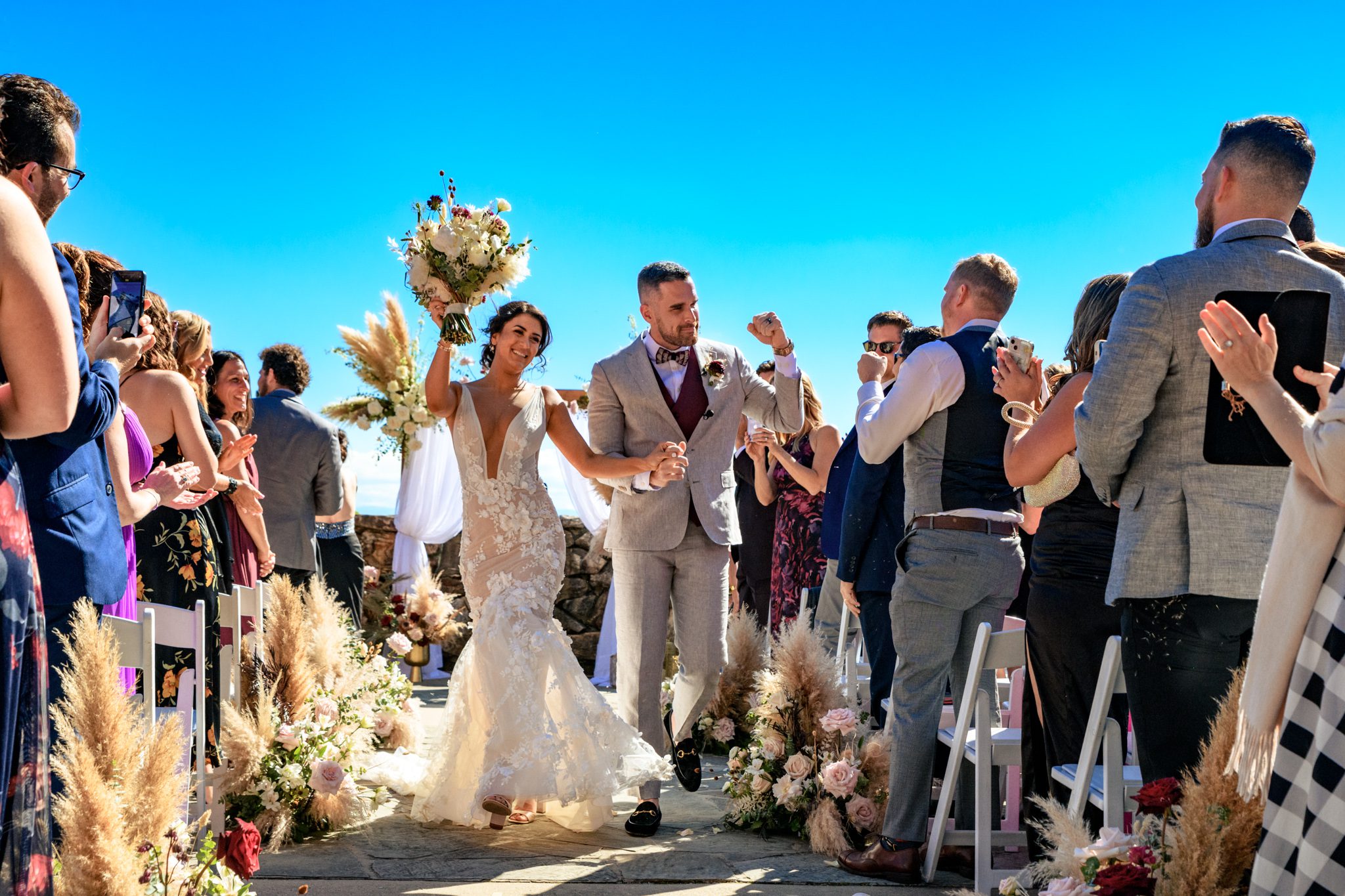 Joyful bride and groom exiting their wedding ceremony on the stunning mountain view terrace at Grove Park Inn, framed by a beautiful floral arch and elegantly decorated aisle