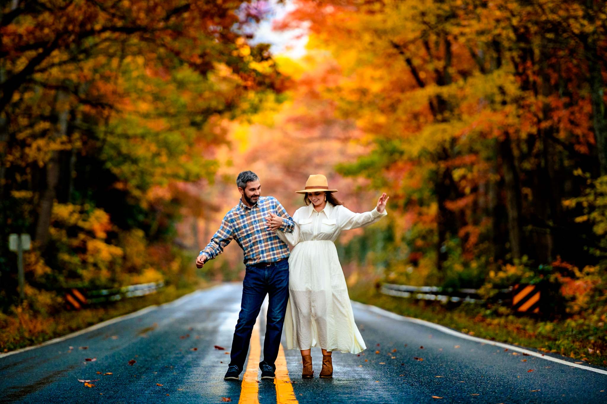 engaged couple dancing in the middle of a road that is lined with fall colors of yellow, orange and red