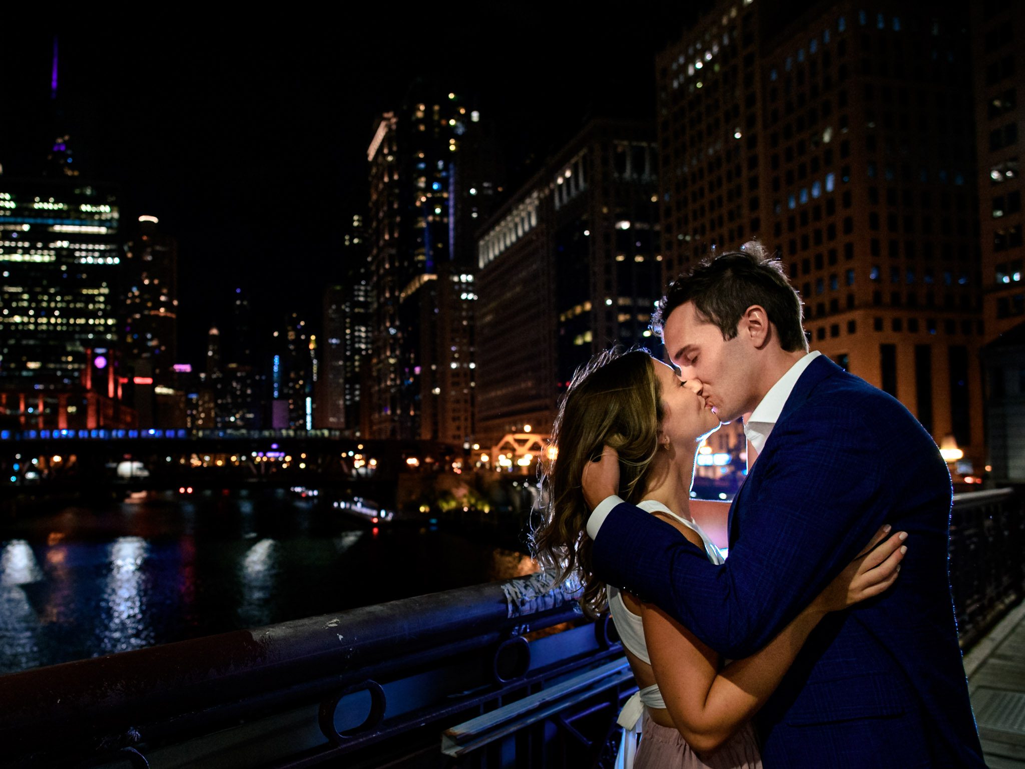 engaged couple dressed up and kissing at night on the lasalle st bridge in downtown chicago for an engagement session
