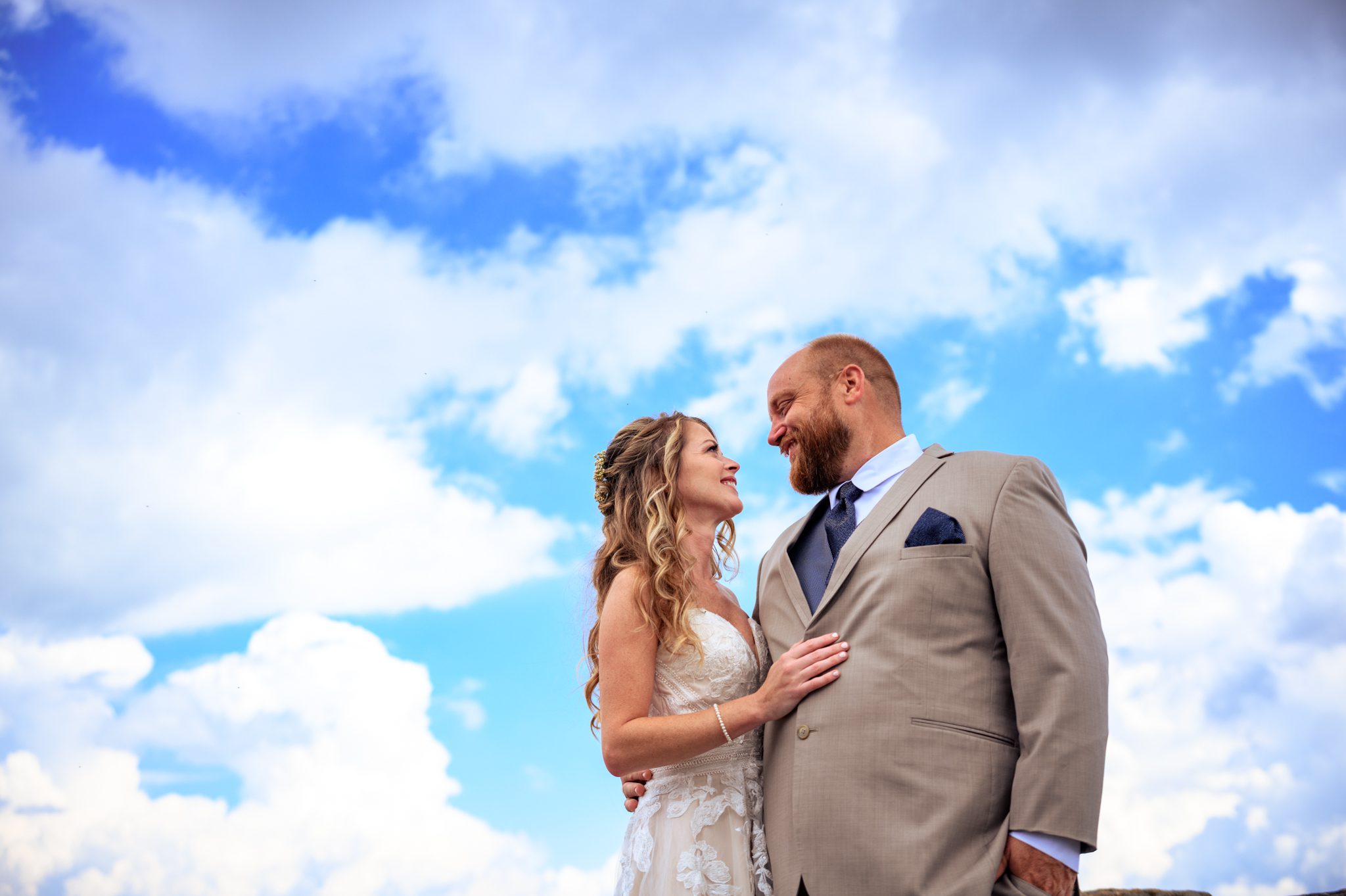 wedding couple with blue sky and clouds behind them
