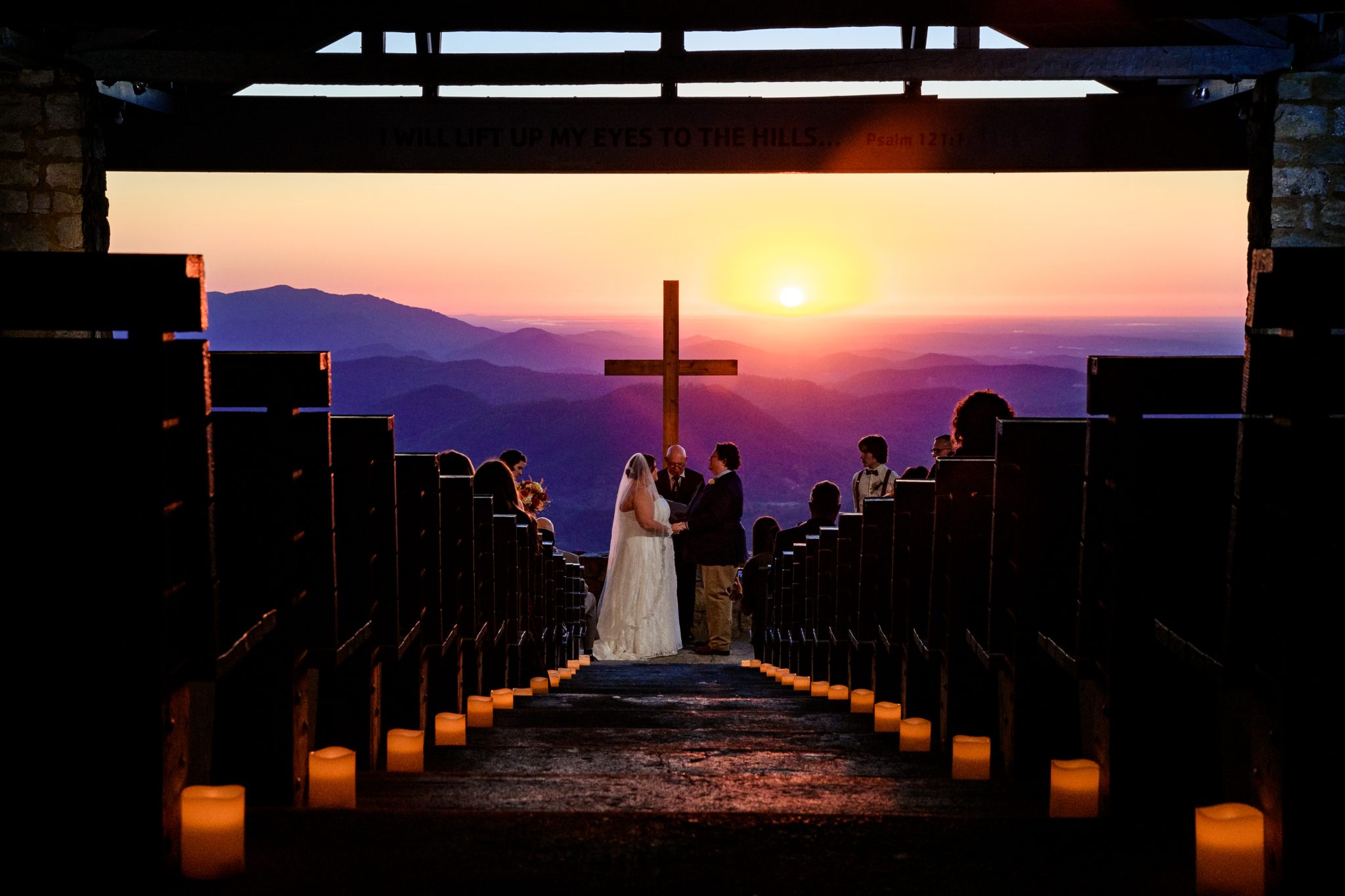 bride and groom stand underneath the cross at pretty place chapel at sunrise