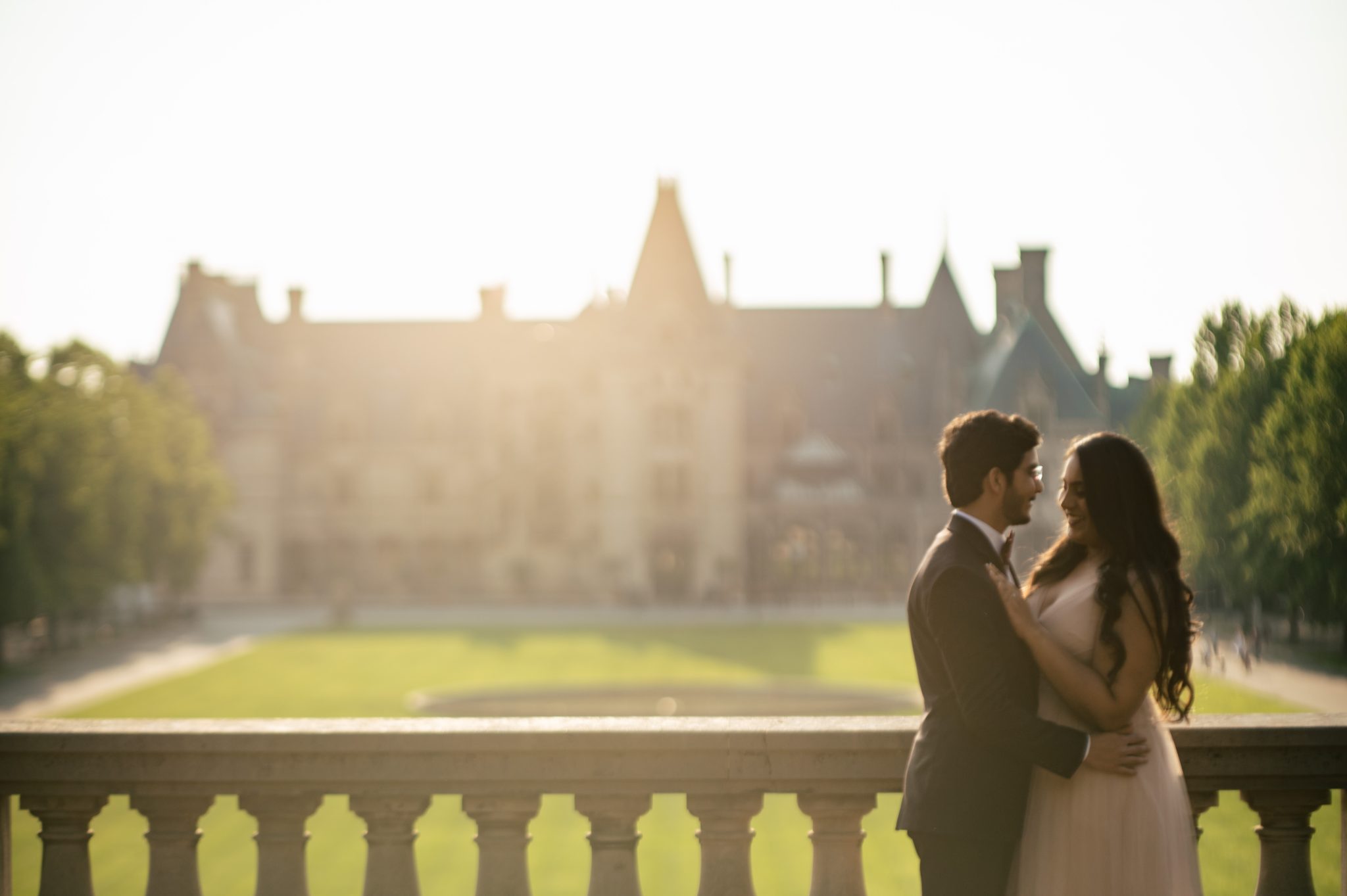 An Asheville engagement photographer captures a bride and groom standing on a balcony in front of a castle.