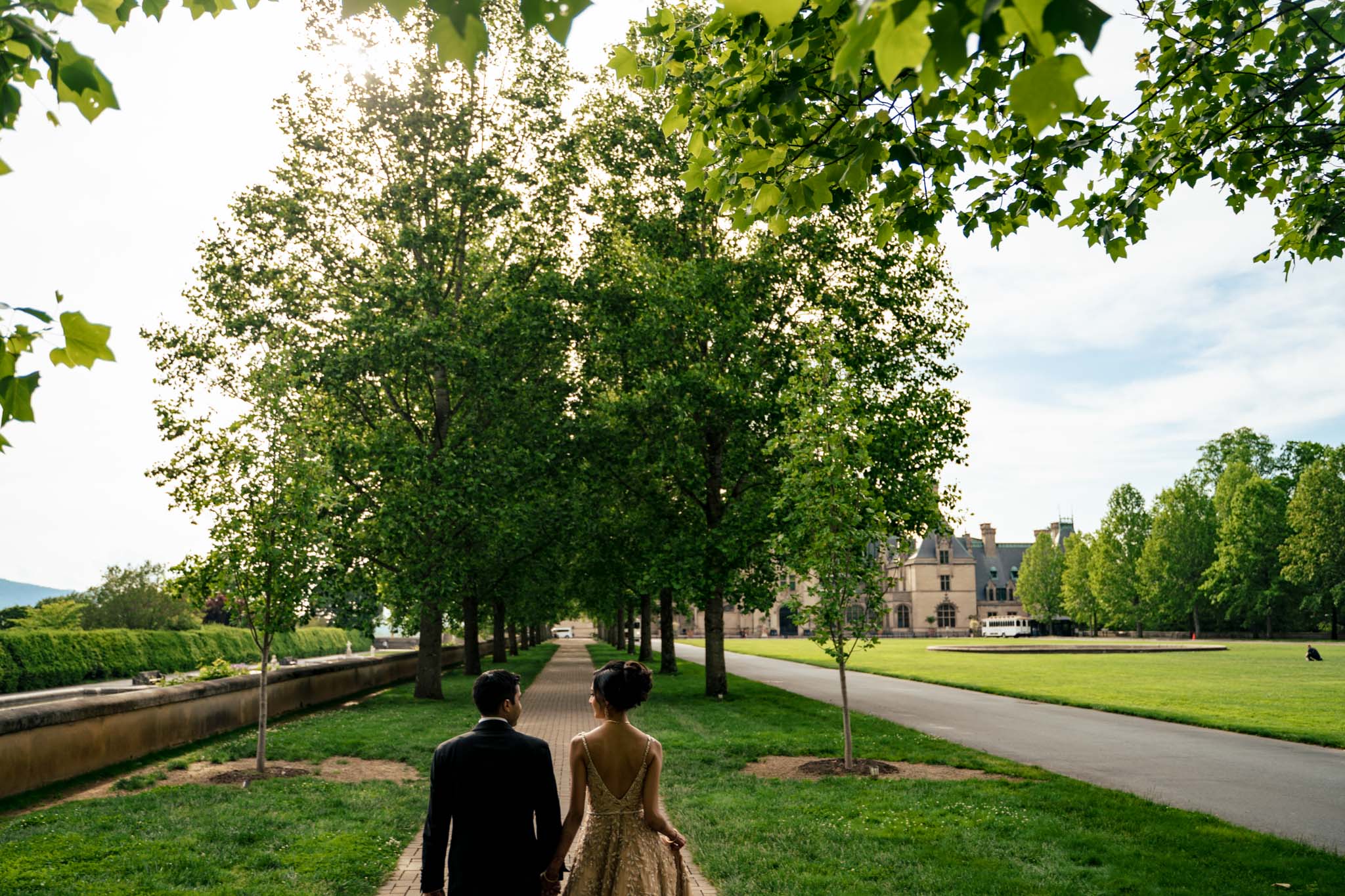 A bride and groom walking down a path in front of the Biltmore Estate.