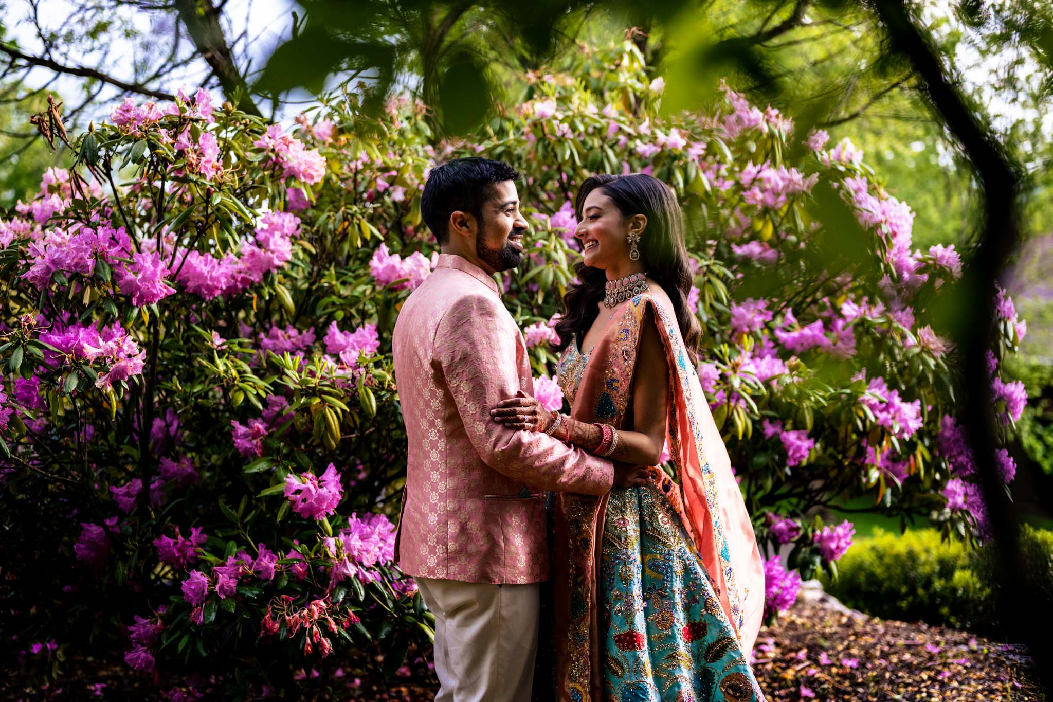 An Indian bride and groom embracing in front of pink flowers at a Biltmore Estate wedding.