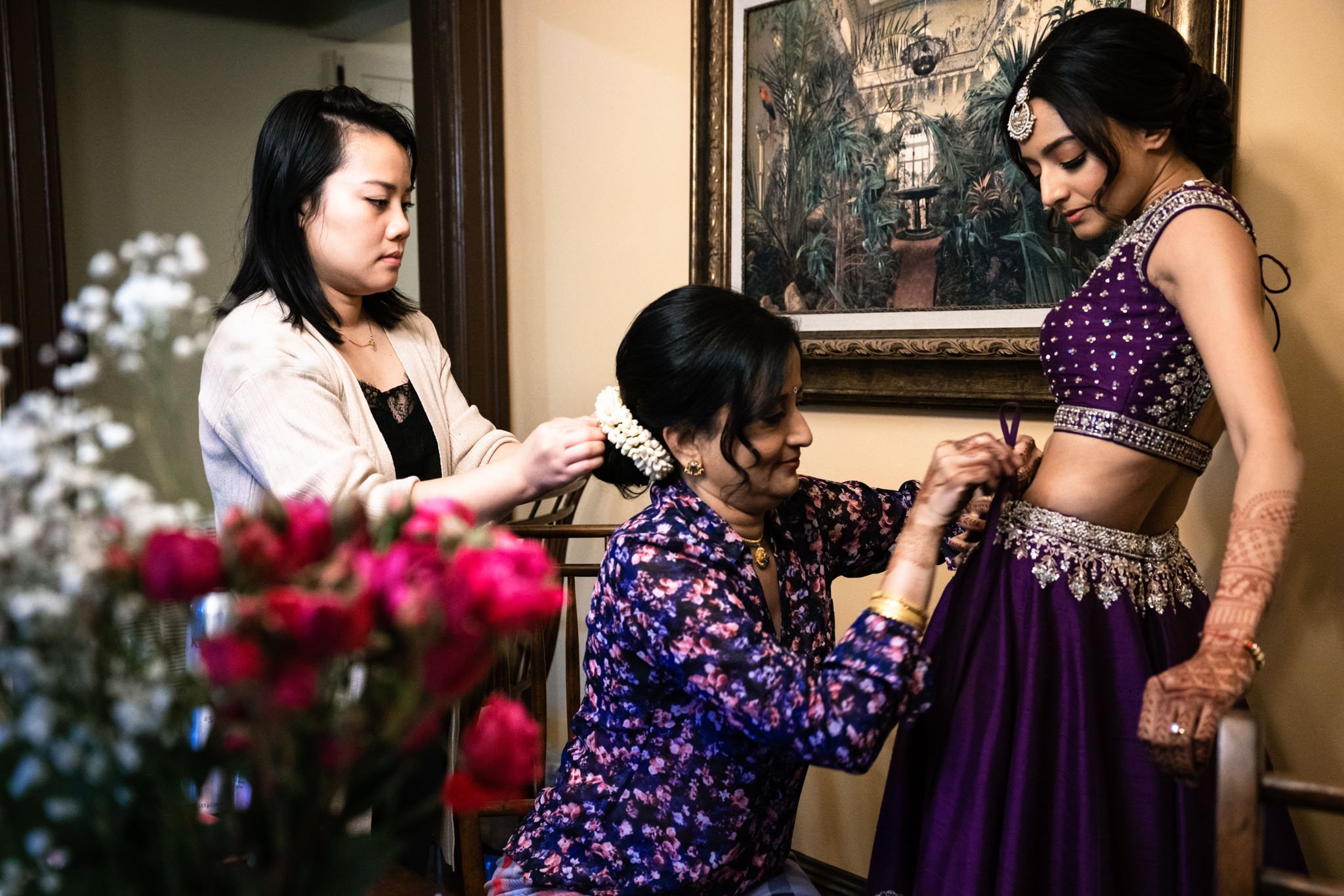 A woman at a Biltmore Estate wedding is helping another woman put on a purple sari.