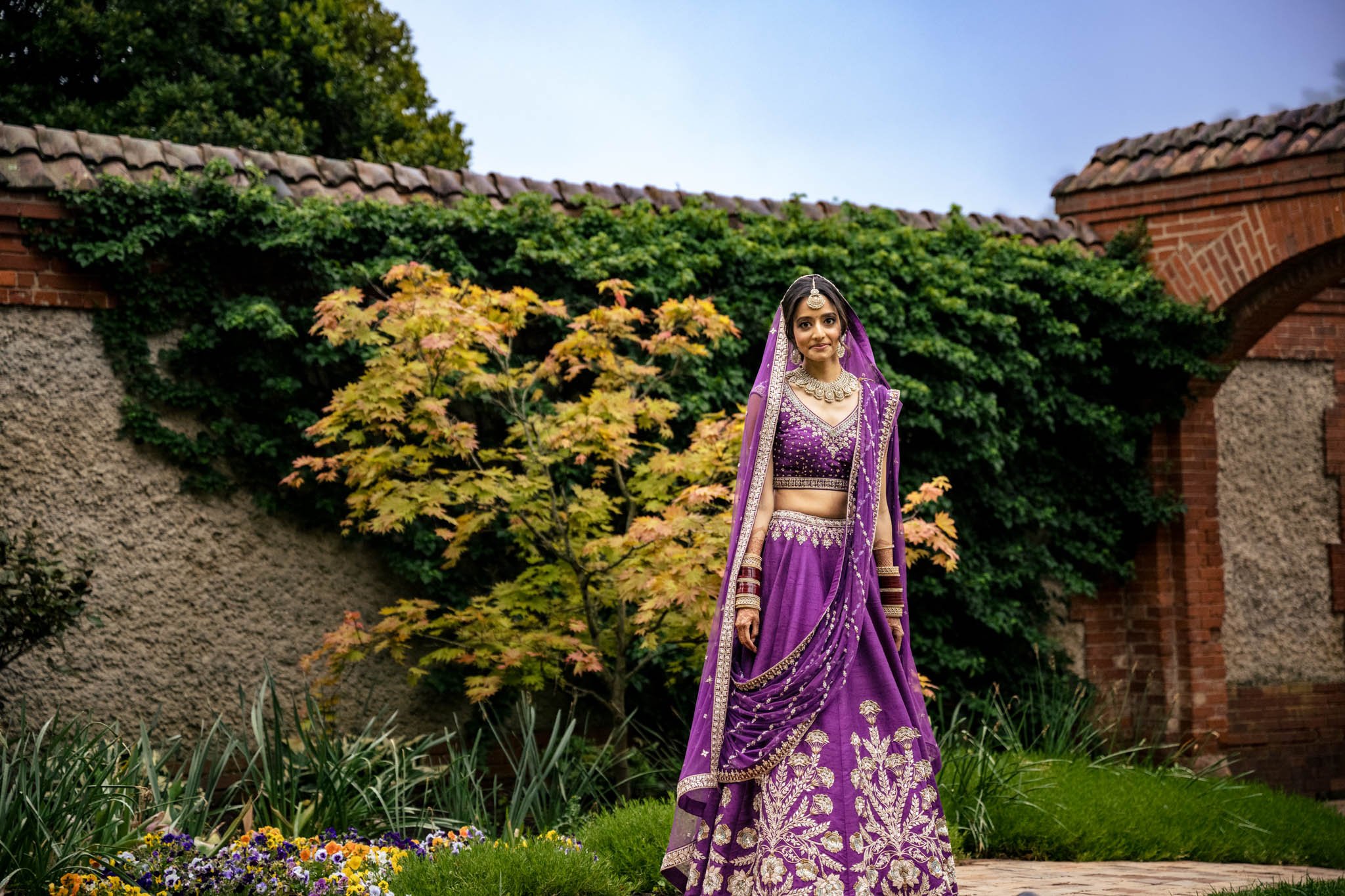 A bride in a purple lehenga posing in the Biltmore Estate garden at her wedding.