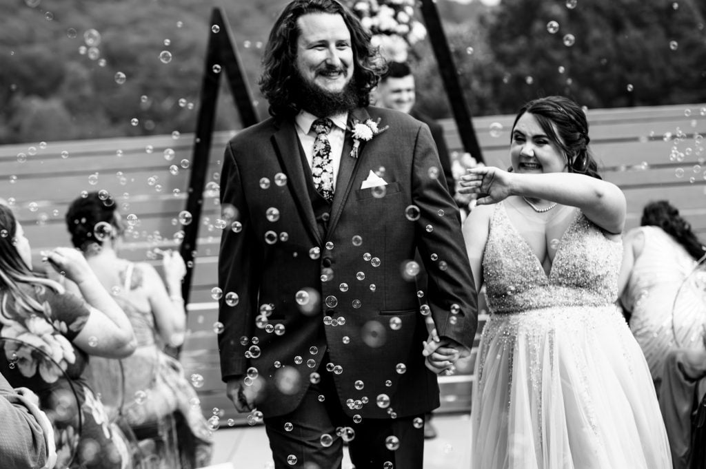 Black and white photo of bride and groom walking down the aisle with bubbles.